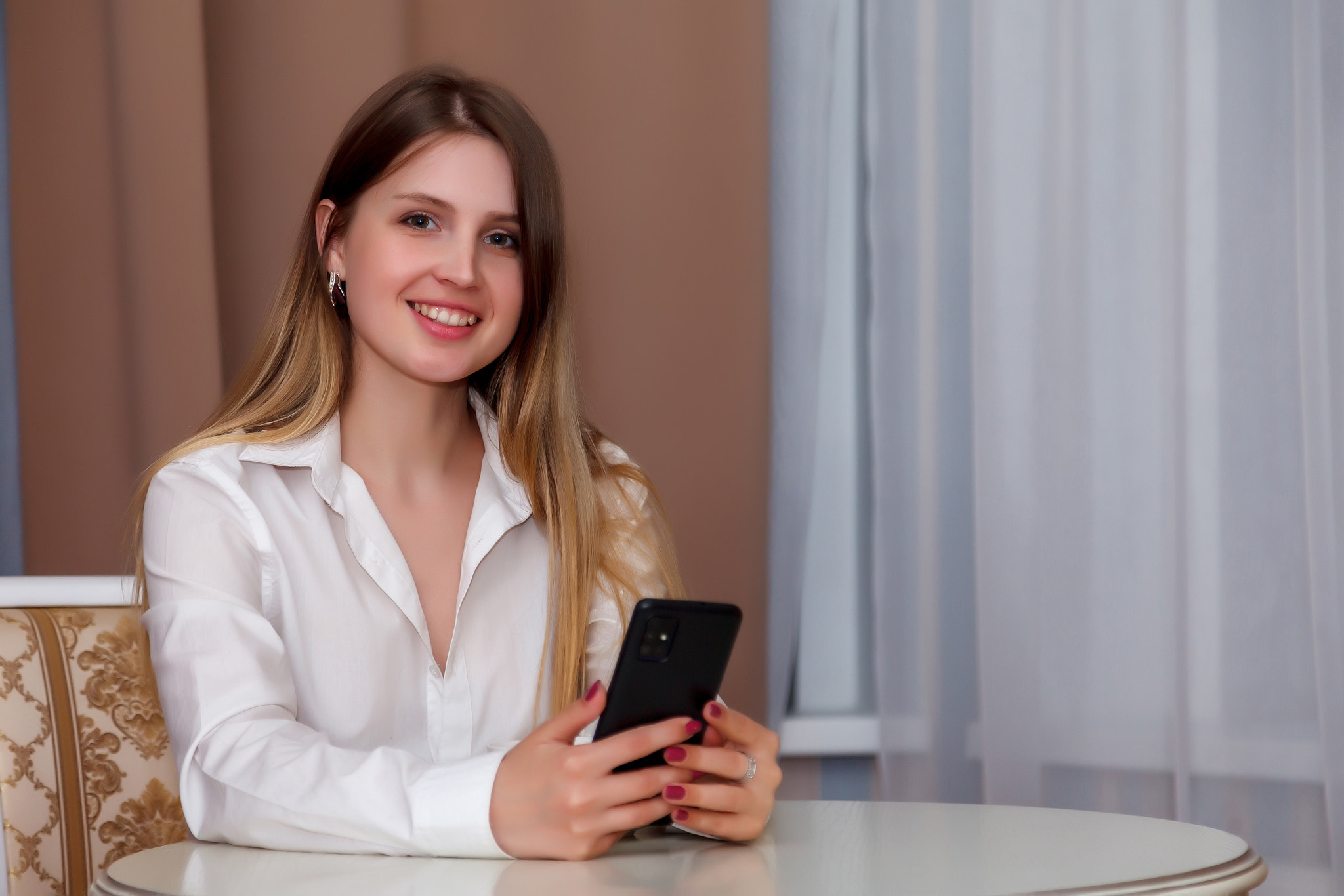 Girl of Slavic appearance with phone and white Cup is sitting at table