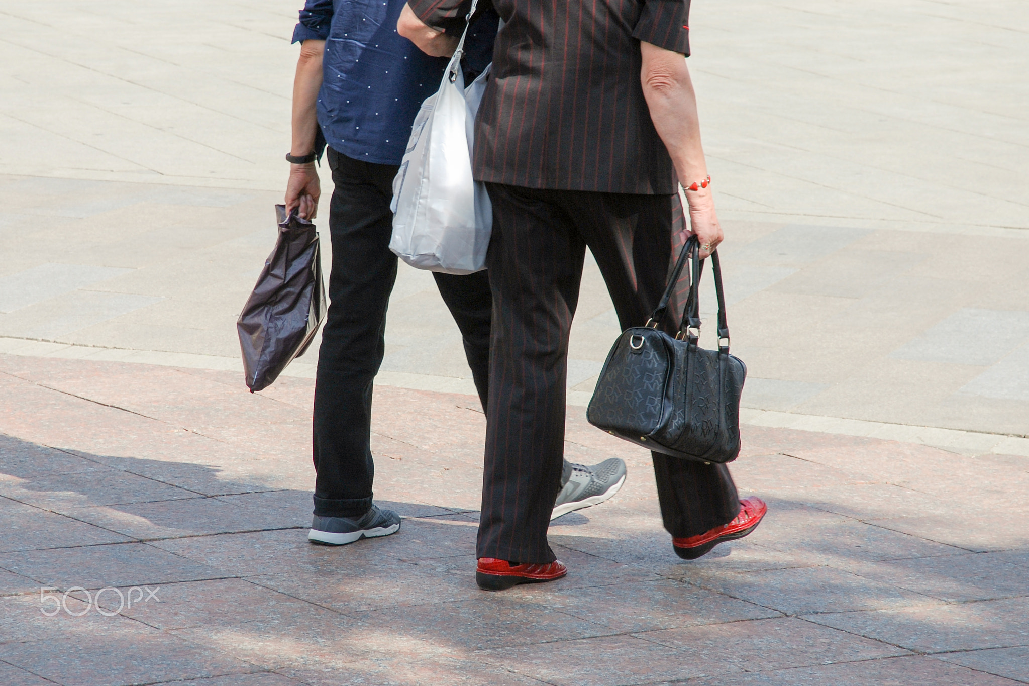 Two elderly women walking across pedestrian area, back view