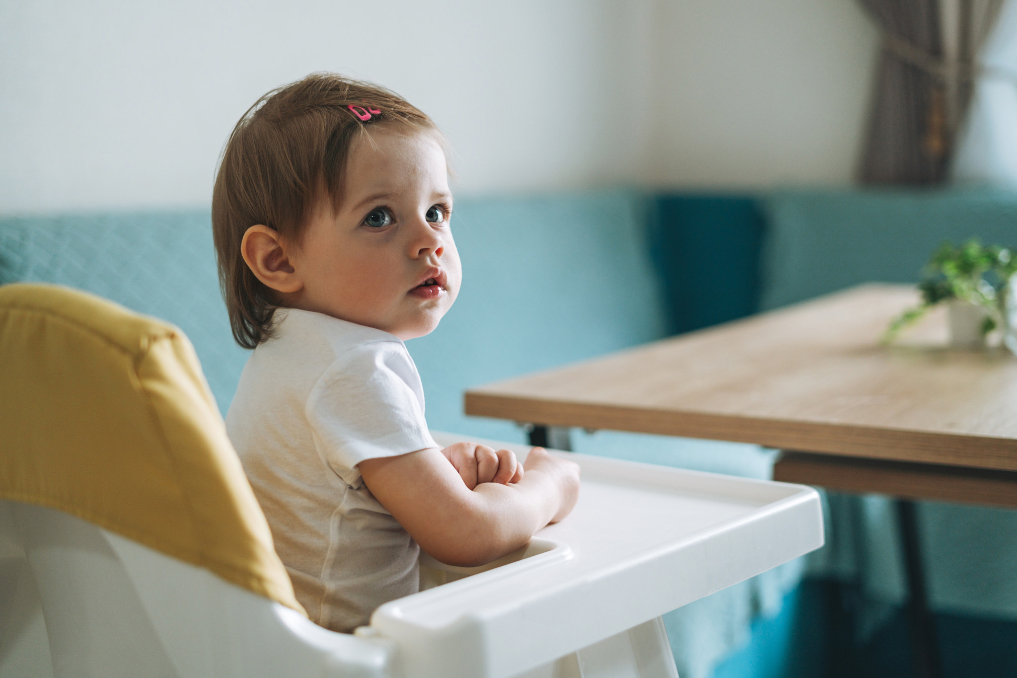 Charming little baby girl sitting in high chair for feeding at the bright kitchen at home
