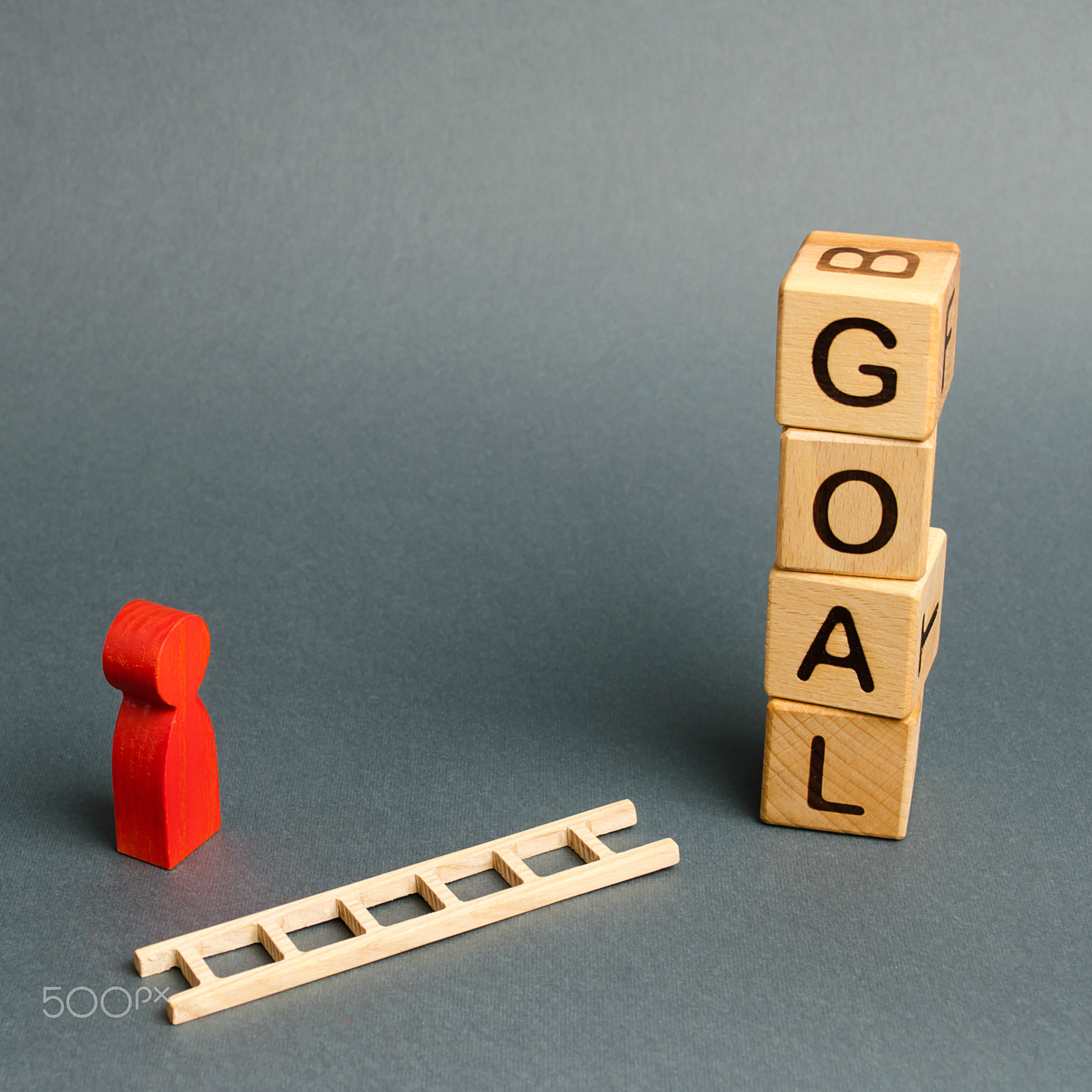 Blocks tower with word Goal and a man figurine with a fallen ladder.