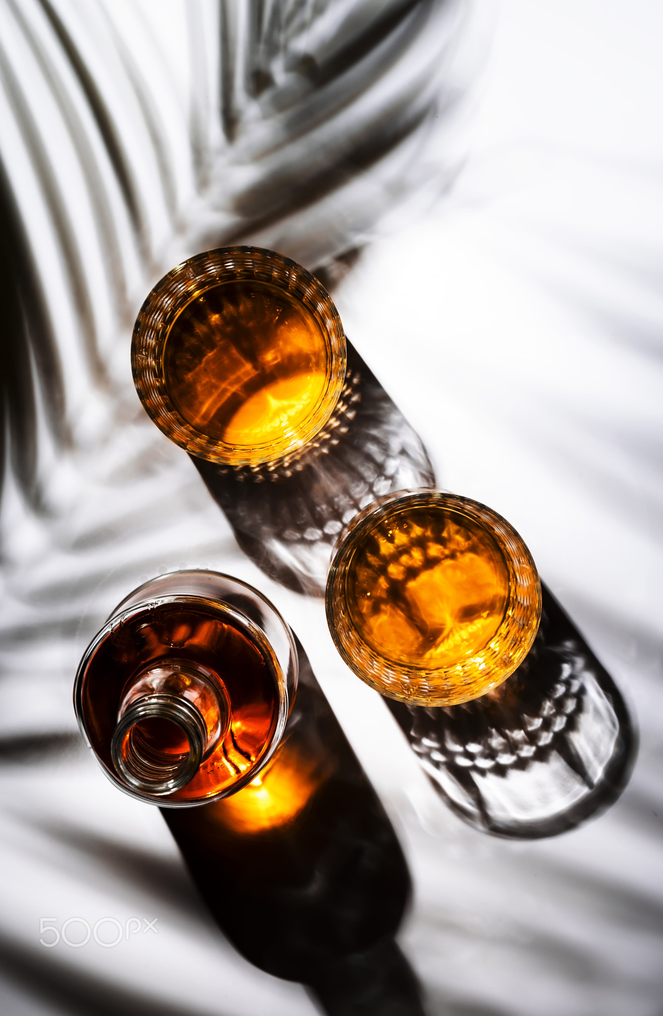 Whiskey in glasses and bottle, white background with hard light, shadows and sun glare, copy space