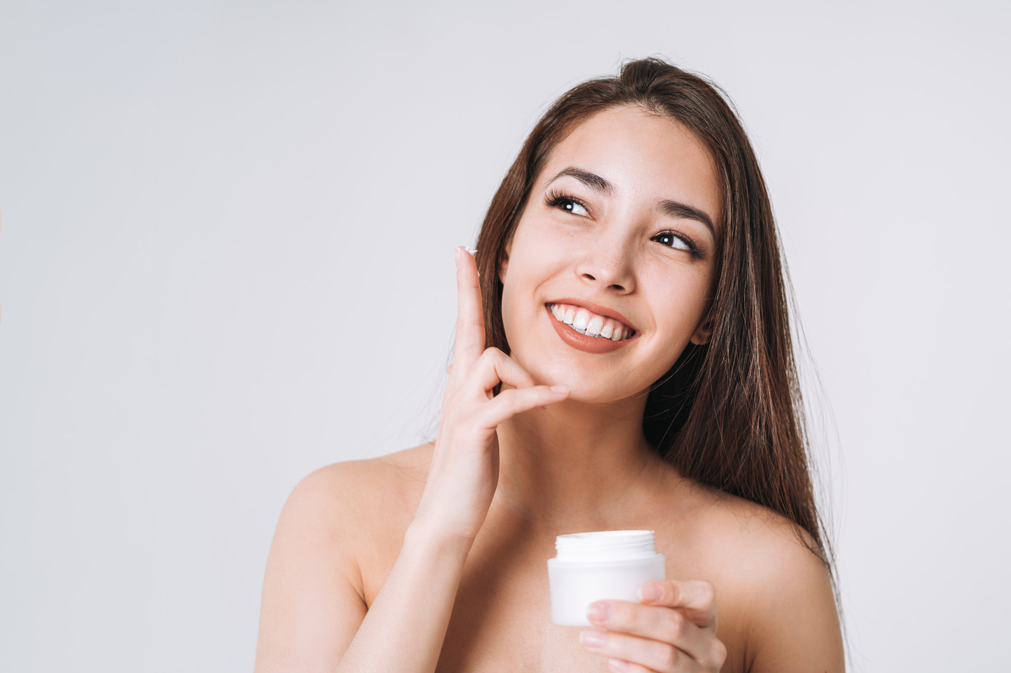 Asian woman put nourishing moisturizer cream on clean fresh skin face and hands on white background