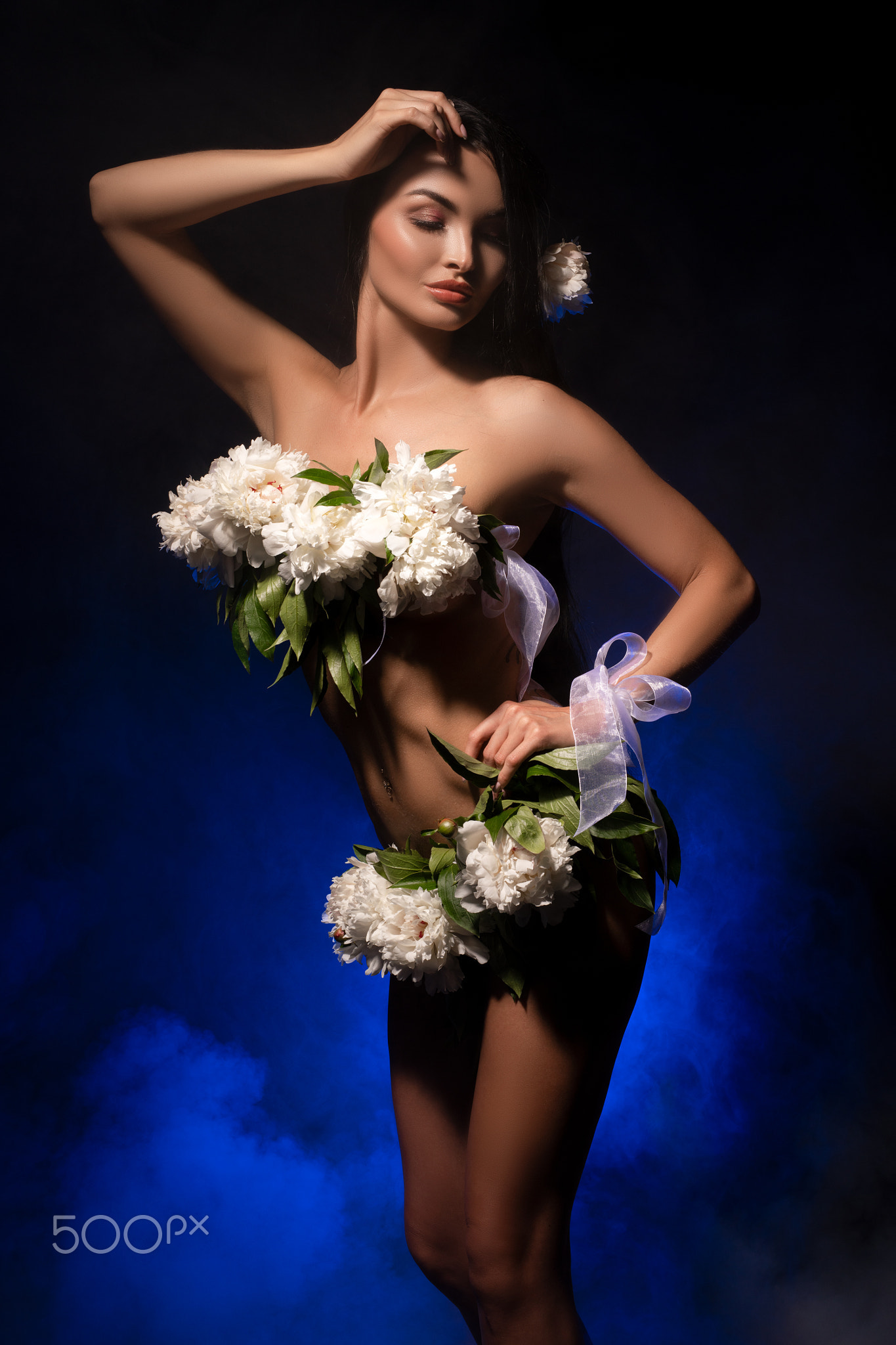 Sensual naked lady with white flowers on body standing in dark studio