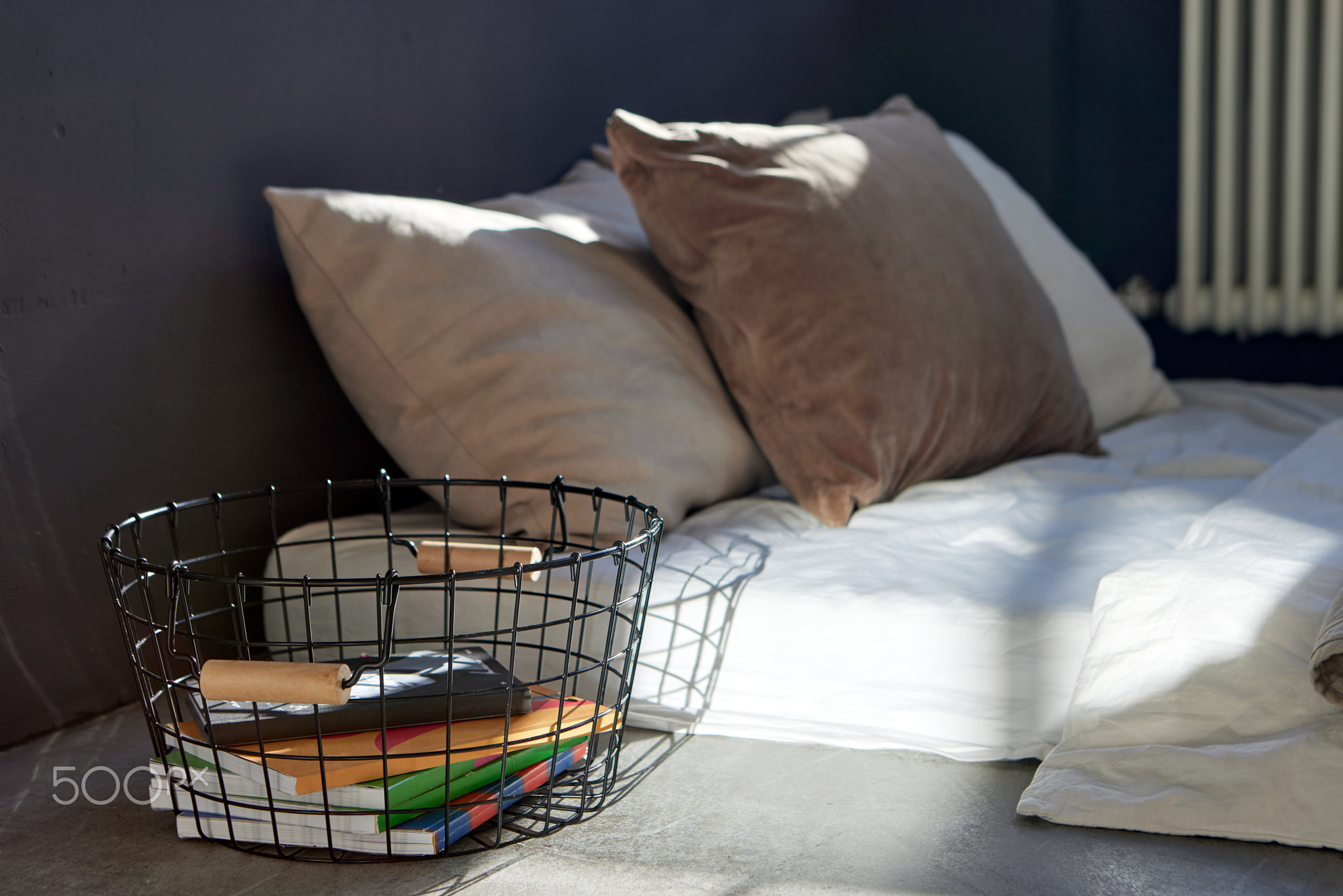 Metal basket with notebooks placed near bed in apartment