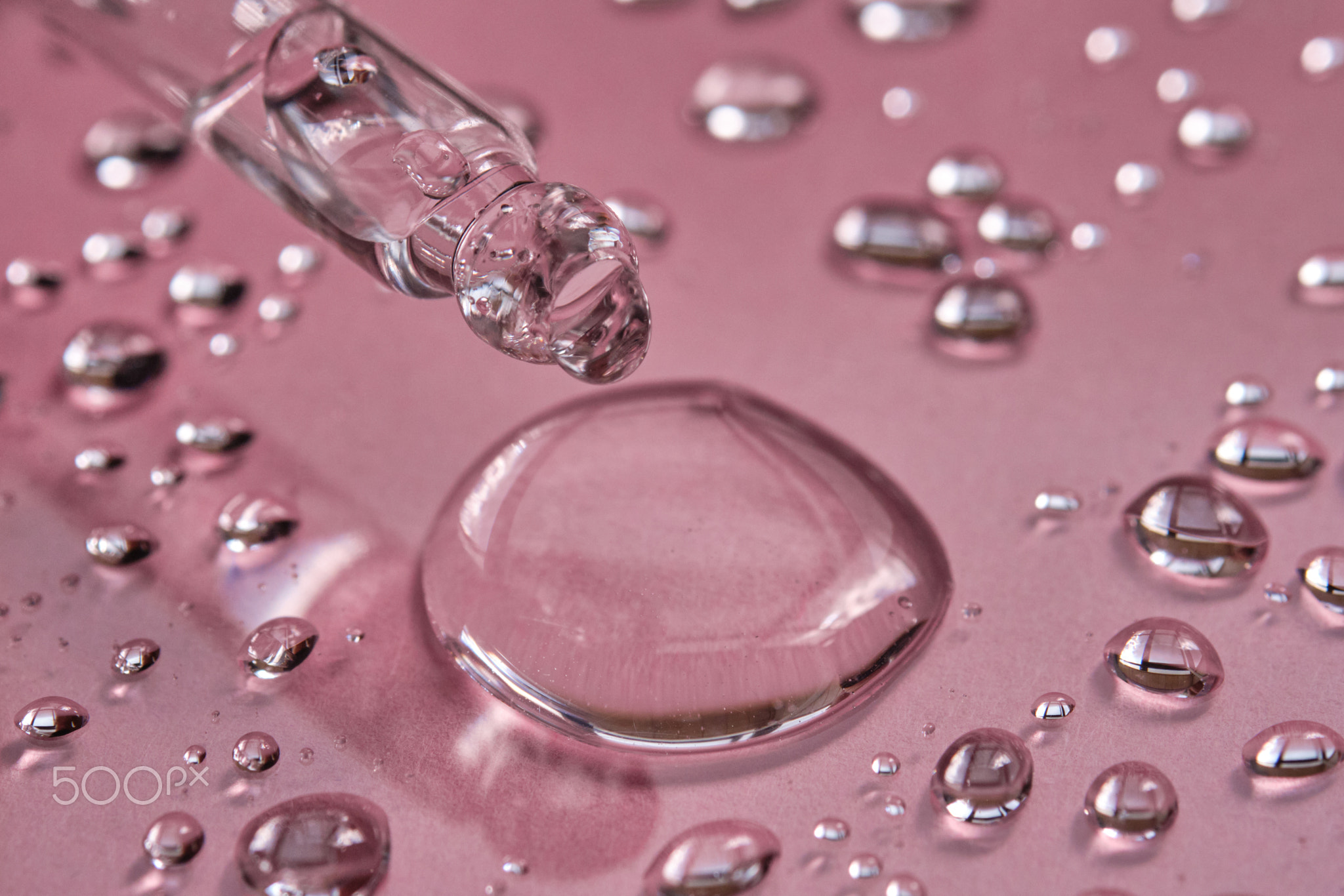 Pipette, drop and splashes of micellar water on a pink background.