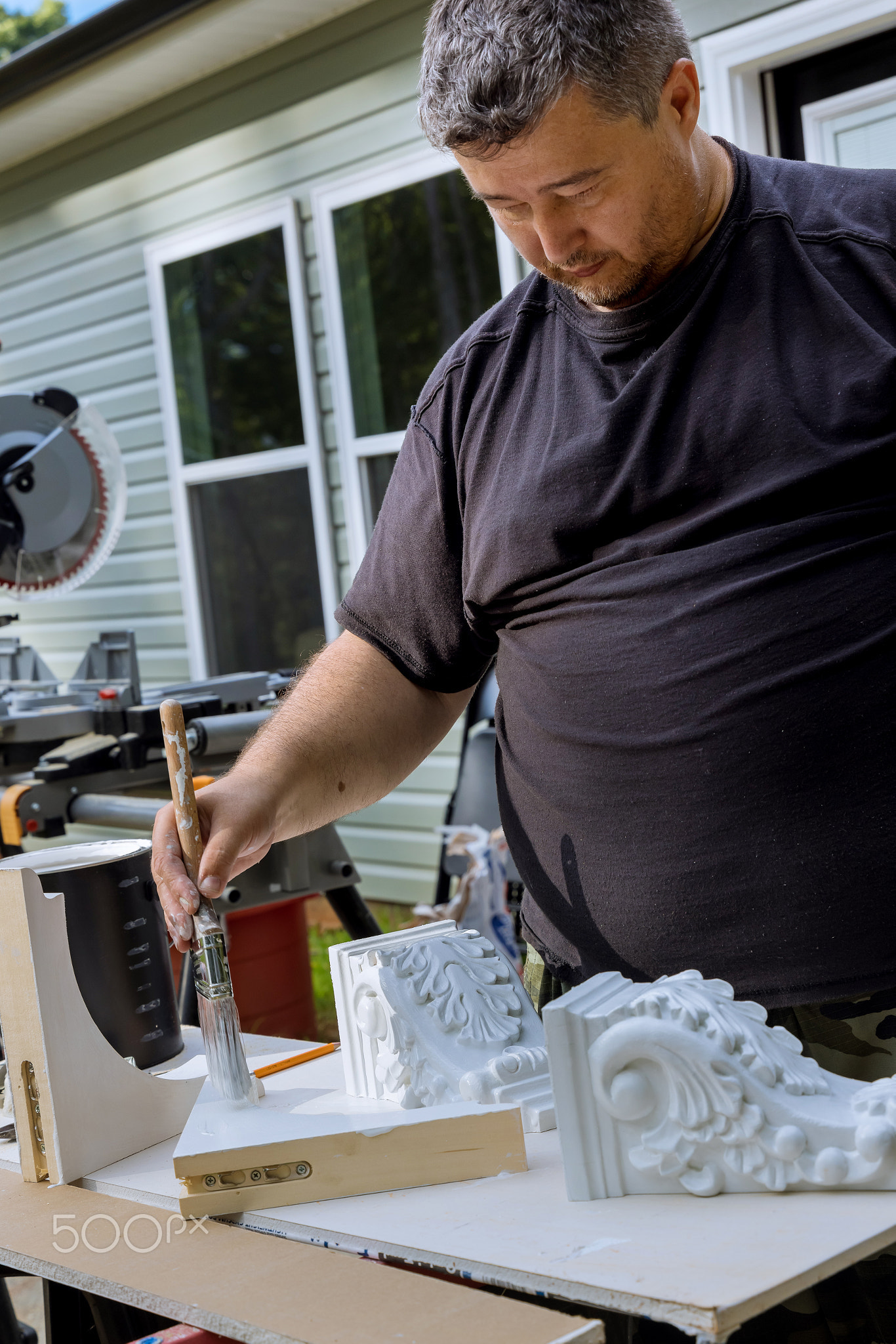 There is a worker painting wooden corbels for the kitchen island that