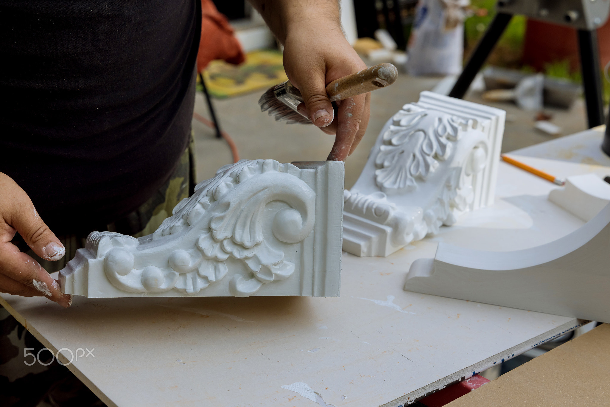 The worker is using a paintbrush to paint wooden corbels for the