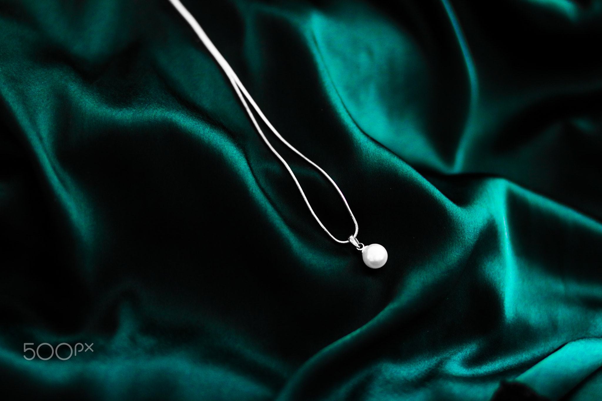 Luxury white gold pearl necklace on dark emerald green silk background
