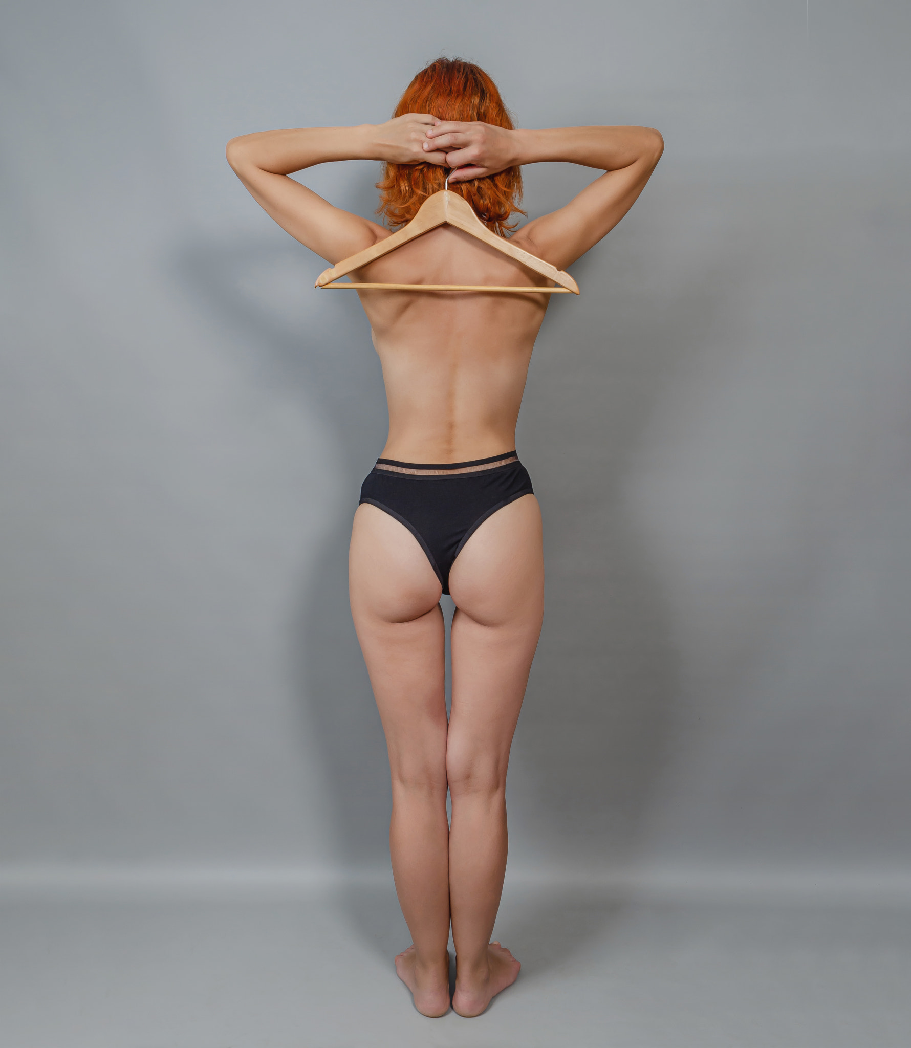 Health of the back, spine. The concept of slimness. A naked young woman holds an empty hanger