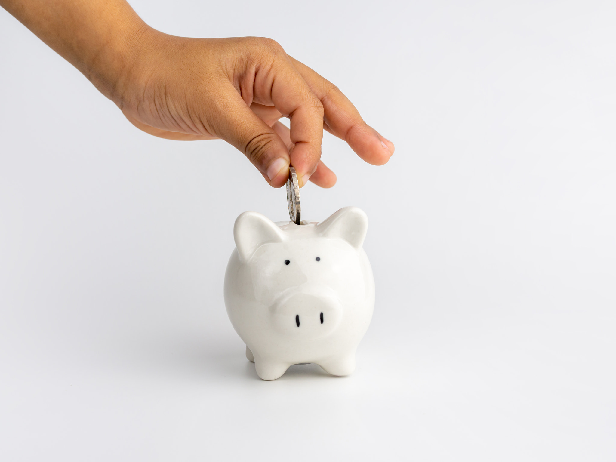 The hand of the coin is dropped into the piggy bank On a white background