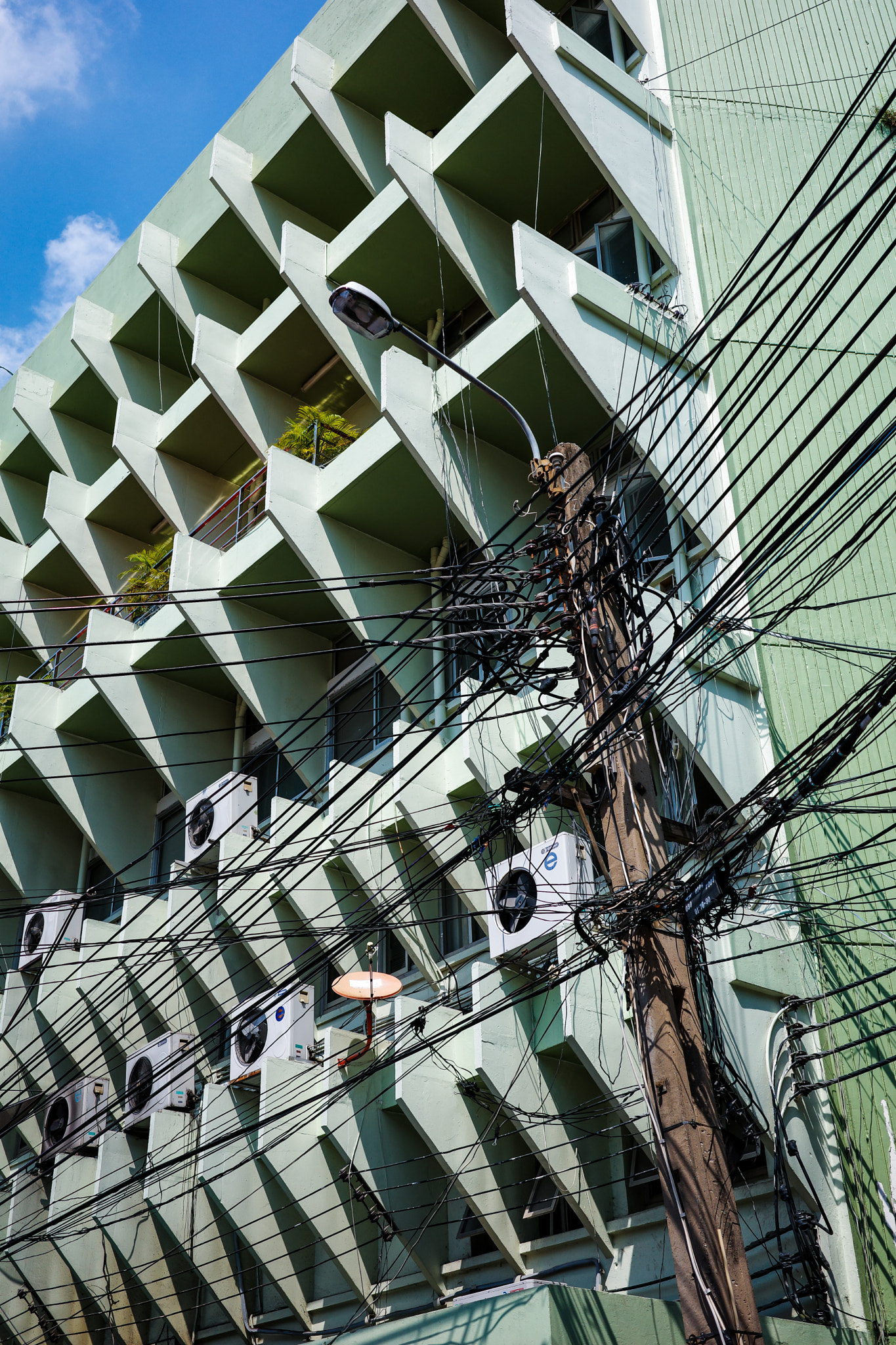 Busy electric wires in front of green building with pattern sunshade.