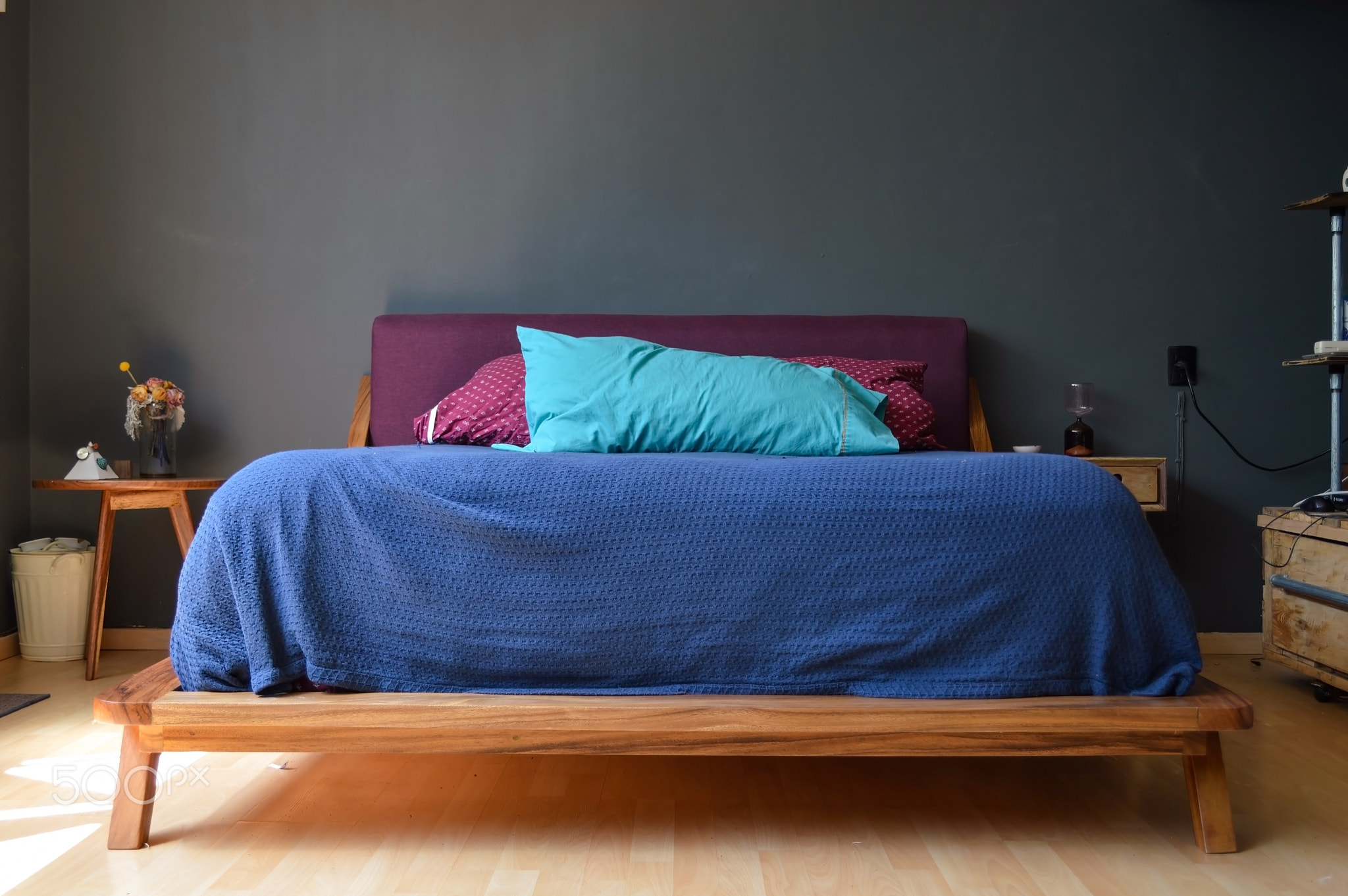 bed base, bedroom with mat on the floor, clay pot in the background, wooden credenza and mirror.