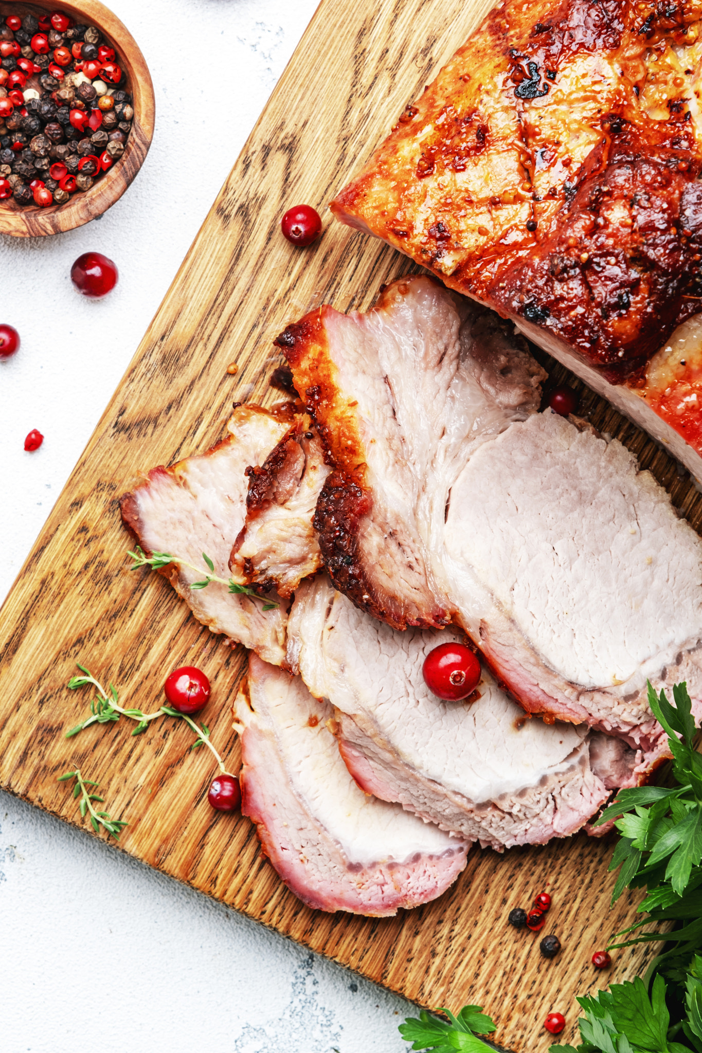 Baked pork loin, whole and cut meat pieces on cutting board with spices, herbs and cranberries