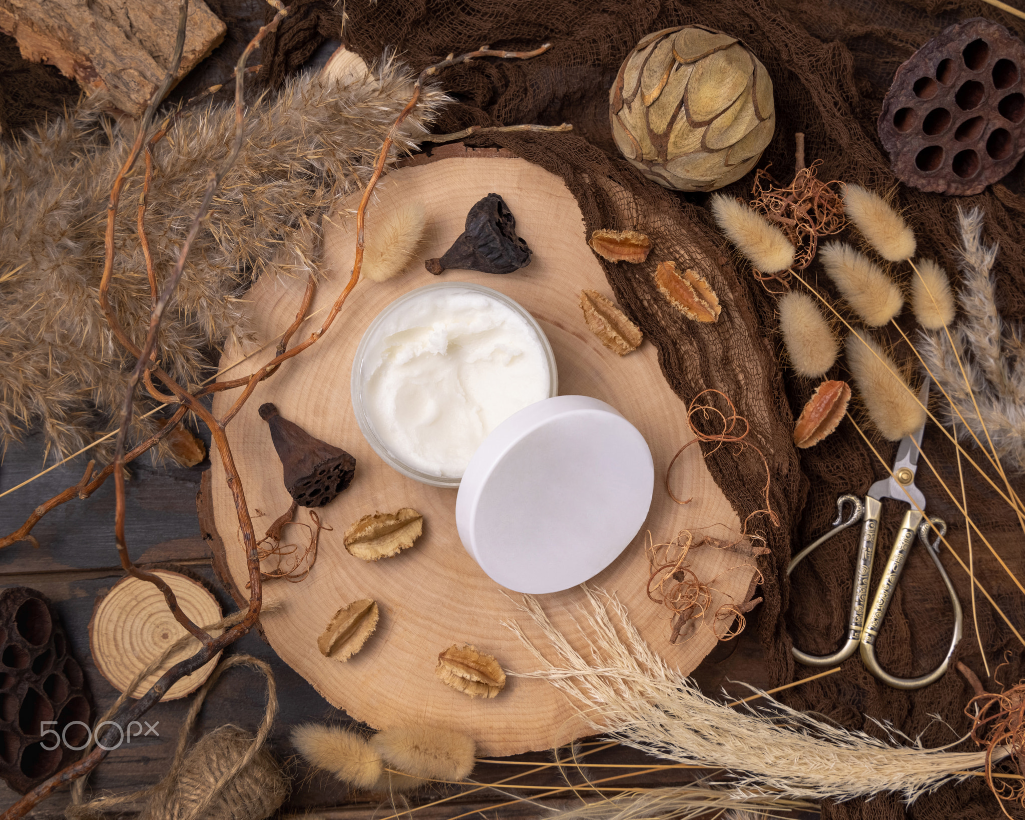 Opened cream jar with blank lid on wood near natural decorations top view. Packaging Mockup