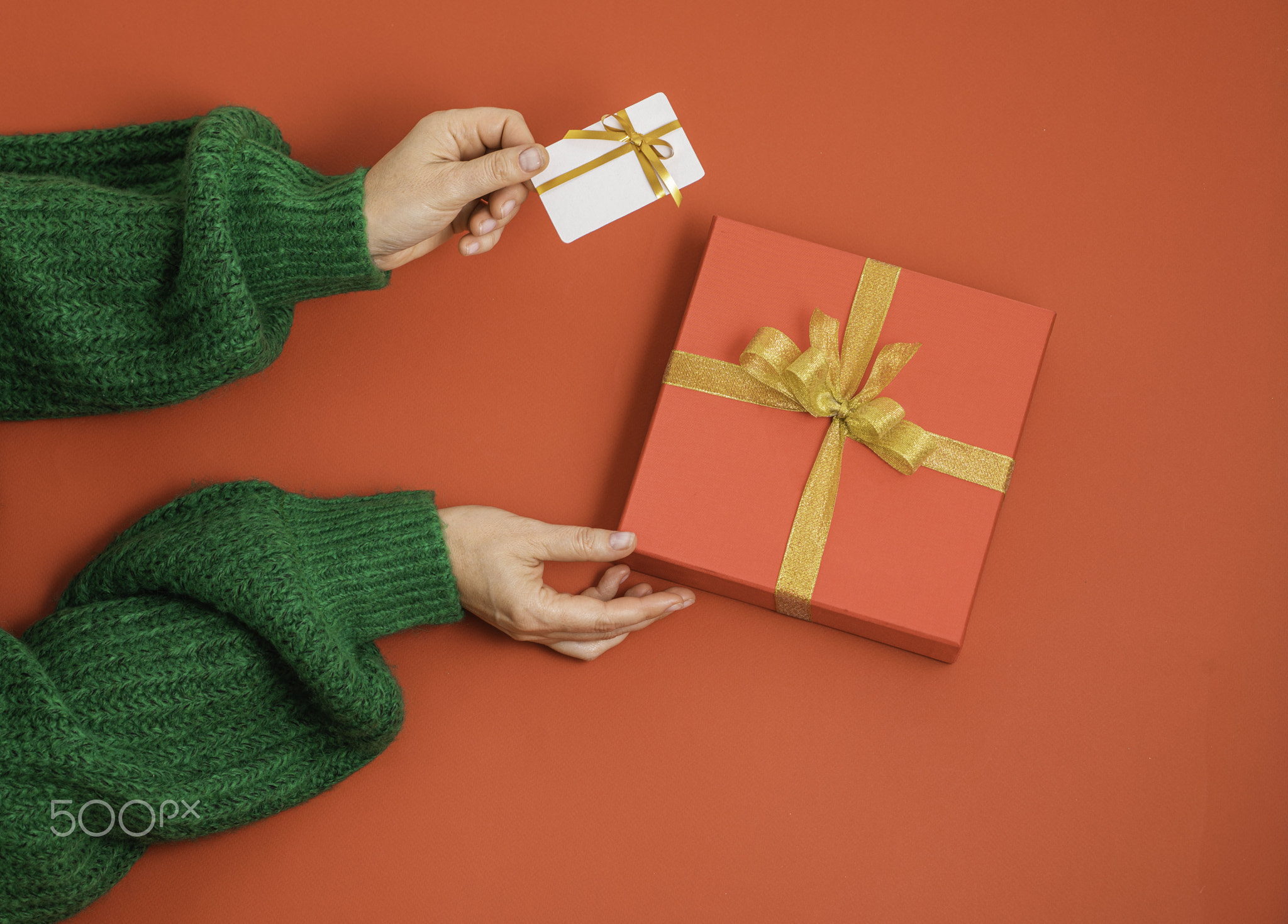 hands holding red gift box with golden satin ribbon bow and white