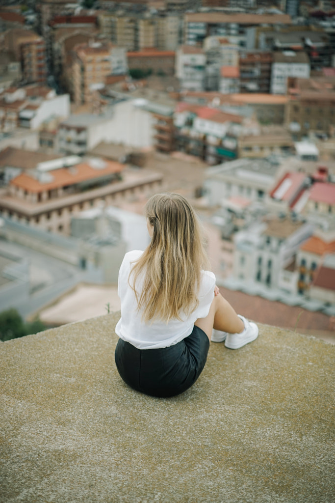 Rear view of woman sitting on retaining wall against cityscape by Olha Dobosh on 500px.com