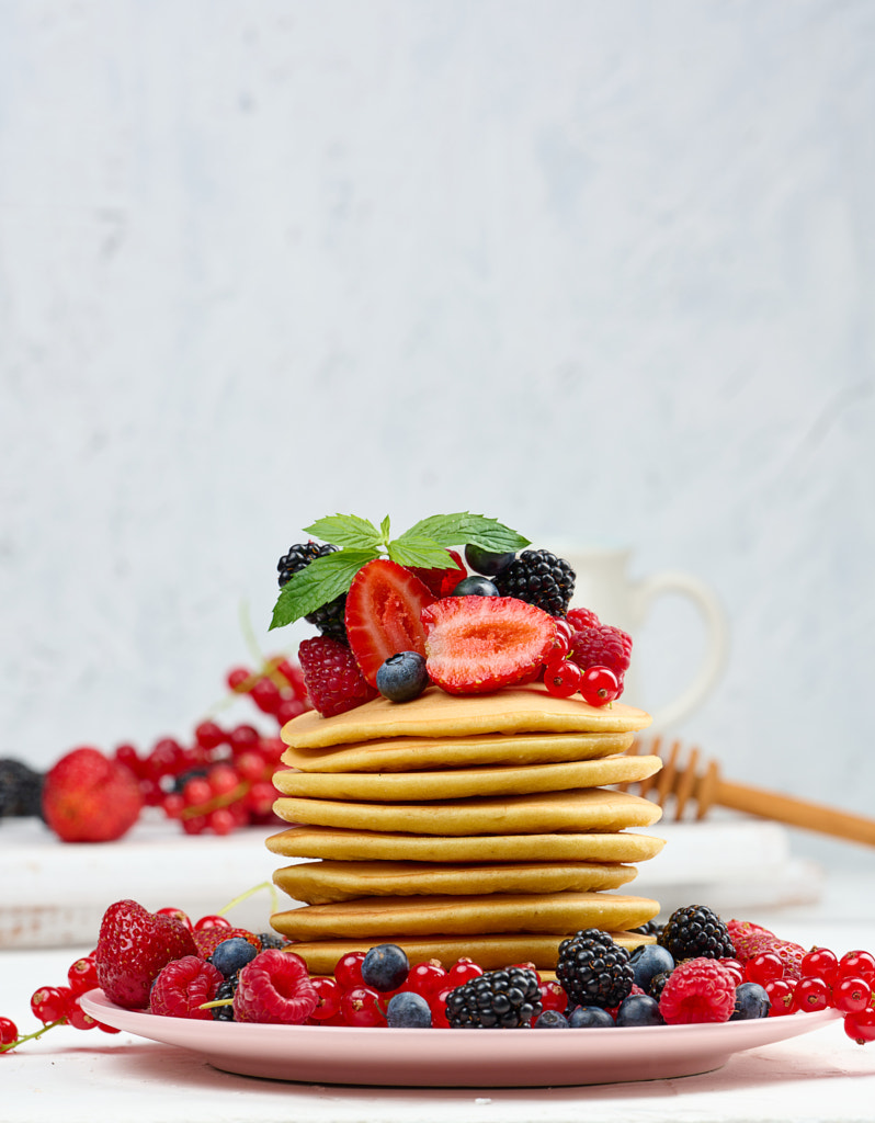 Stack of baked pancakes with fruits in a round plate on a white table ...