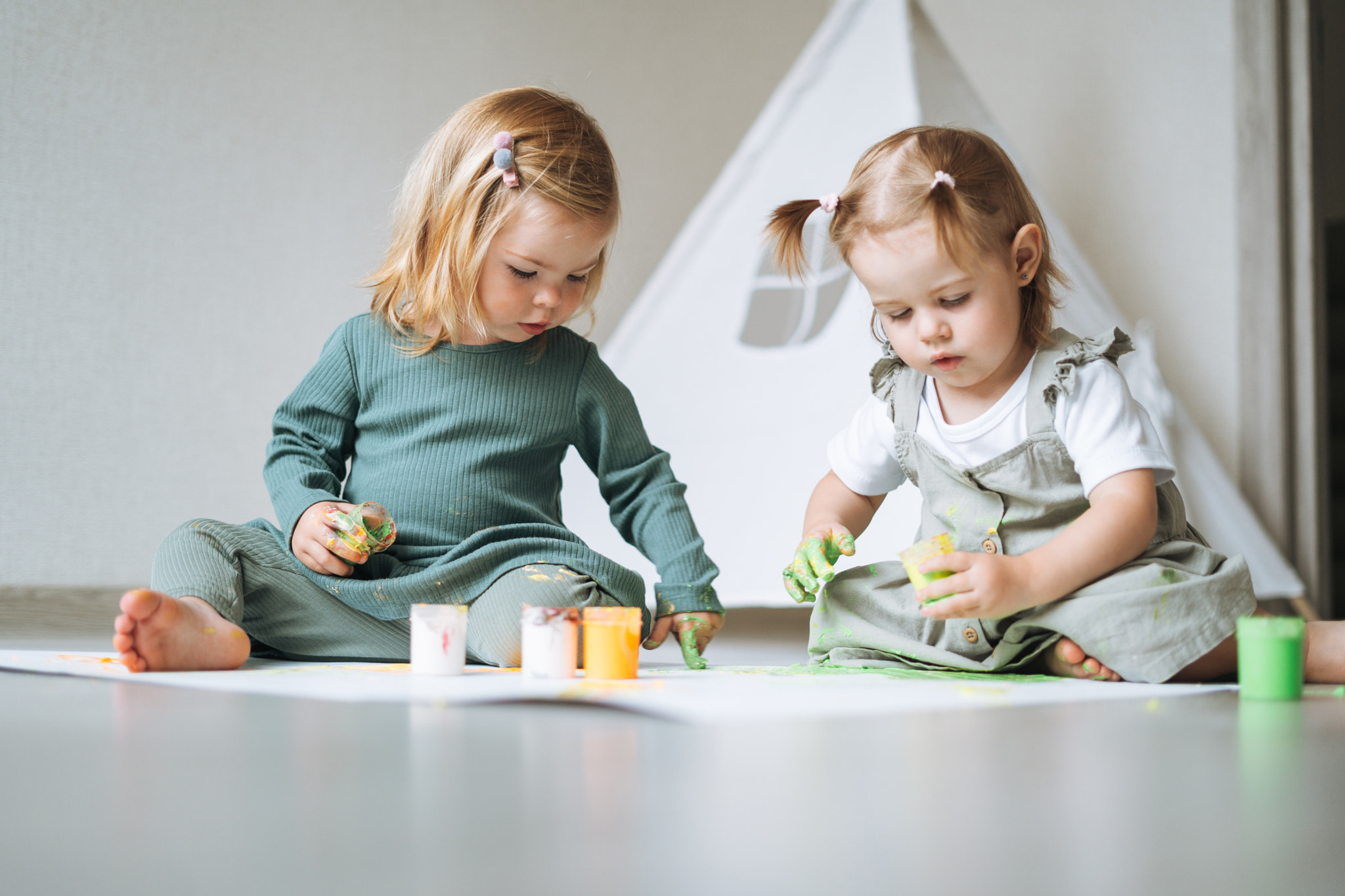 Two little baby girls twins sisters playing with finger paints in the children's room at home