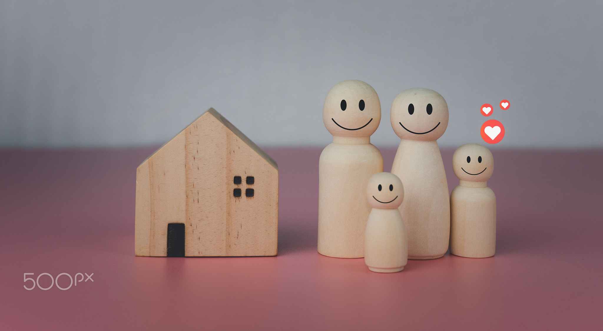 Model house with wooden dolls standing lined up on pink background and heart icons.