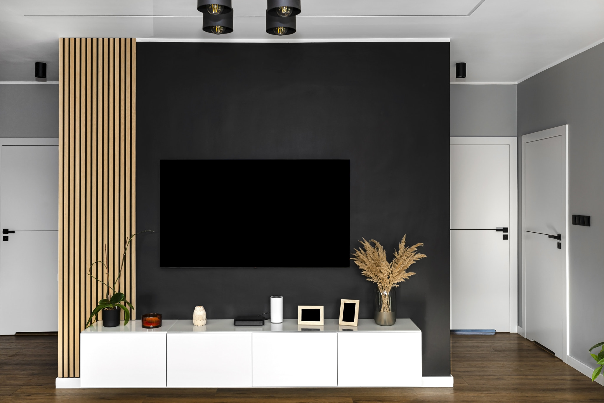 Black matte TV wall in the living room with a hanging TV set over a white wall unit.