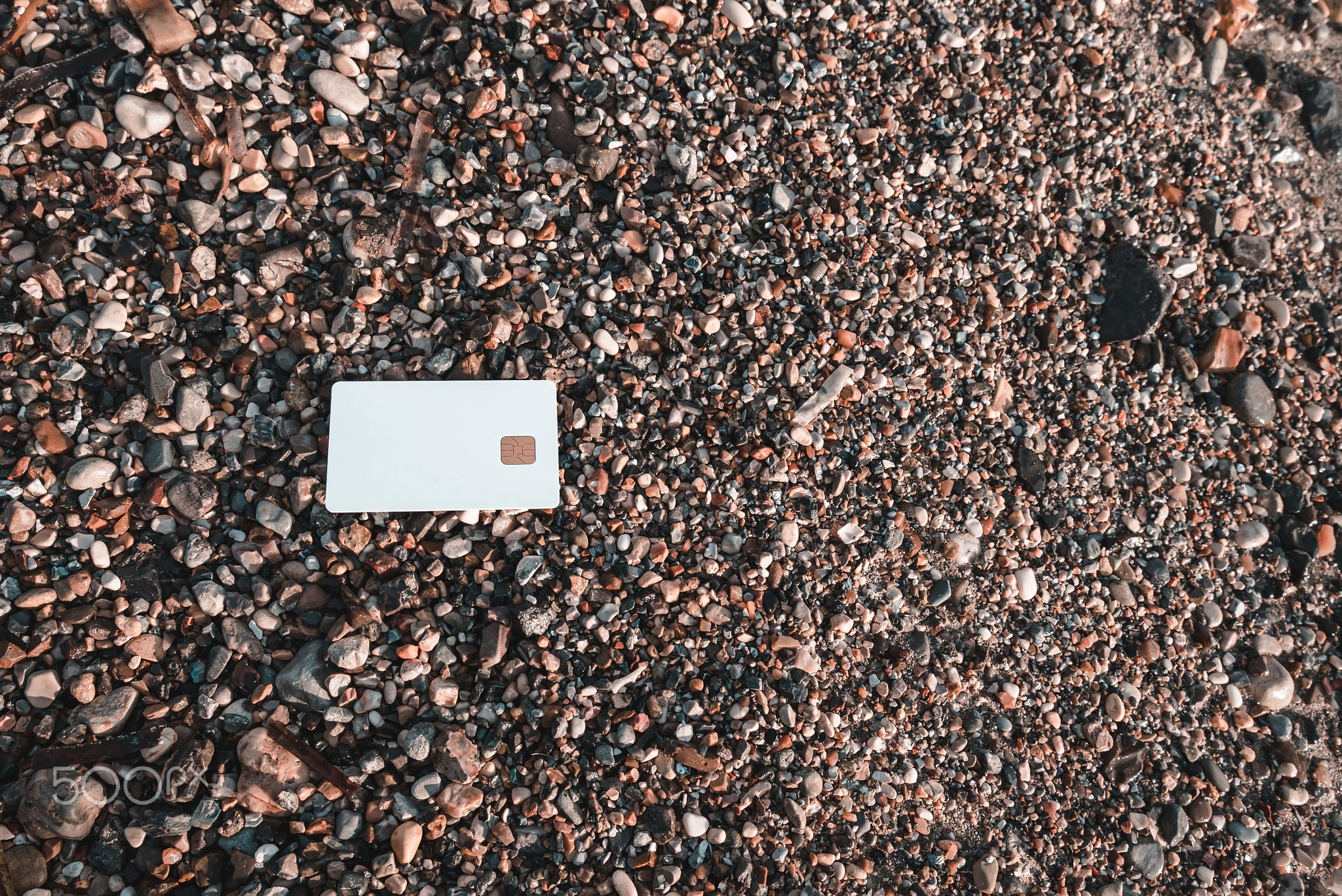 White Bank Card Lies On Sand And Pebble Beach On Sunset Moraitika