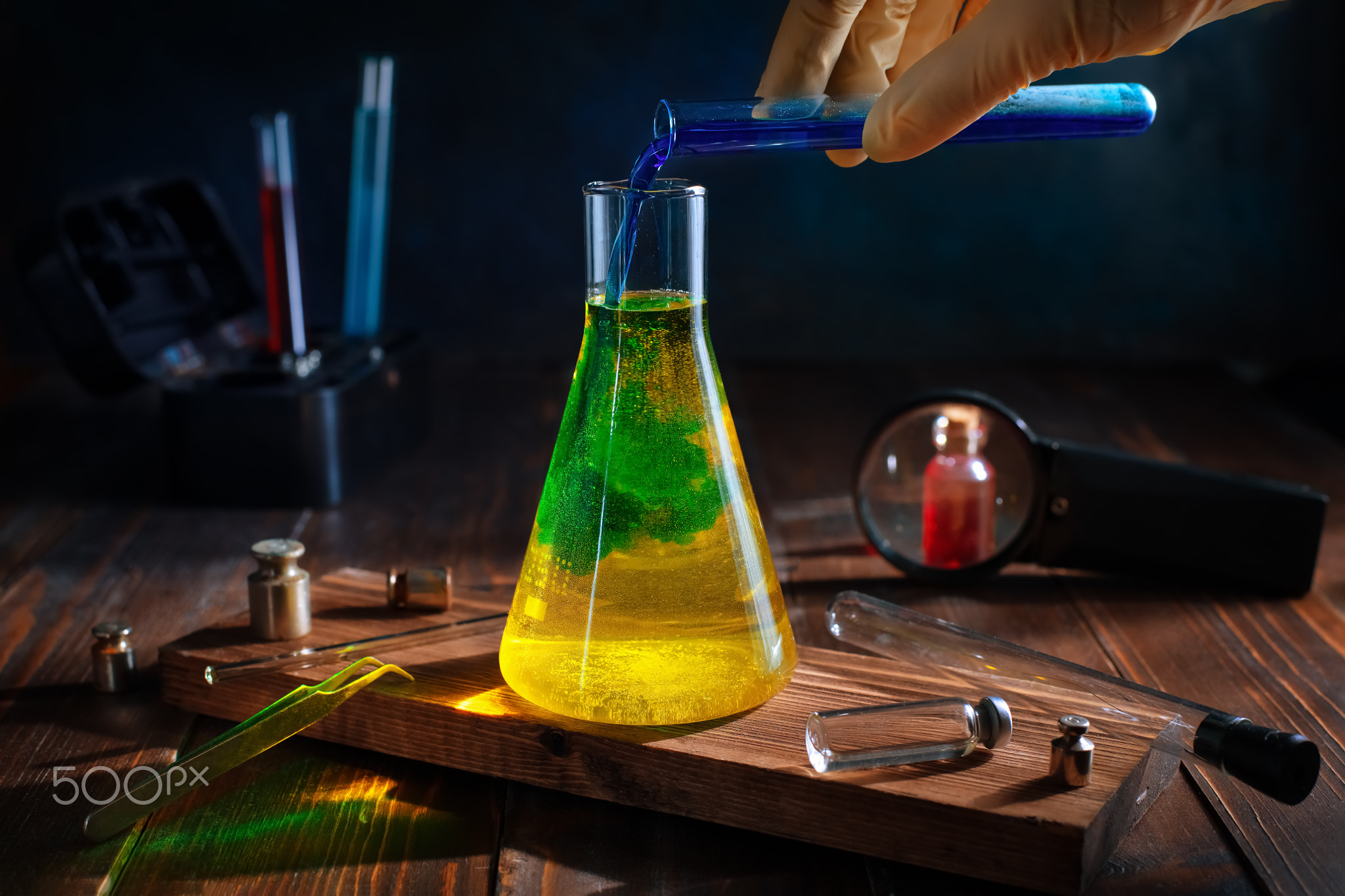 scientist pours blue liquid into yellow in a chemical flask