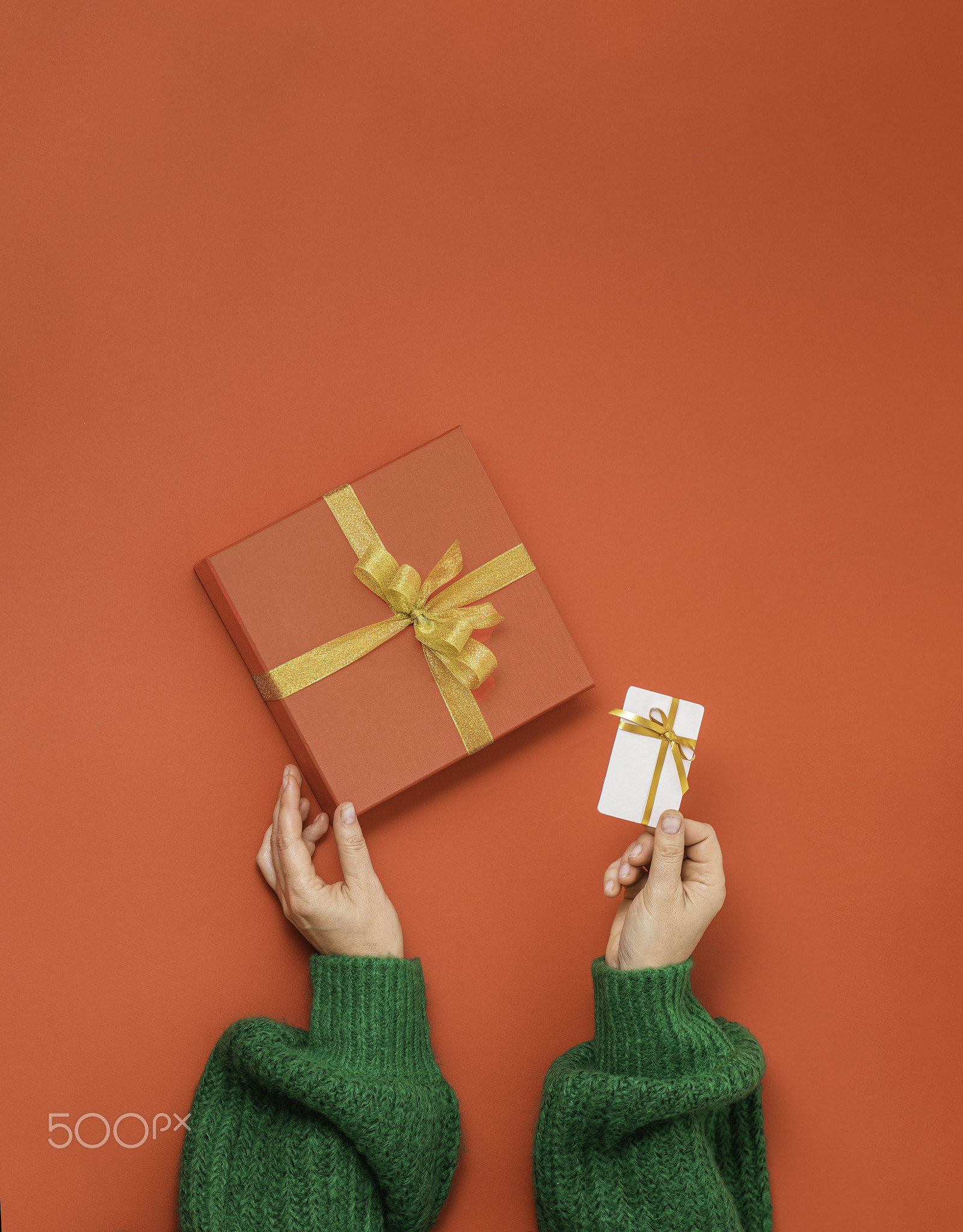 hands holding red gift box with golden ribbon bow and white plastic