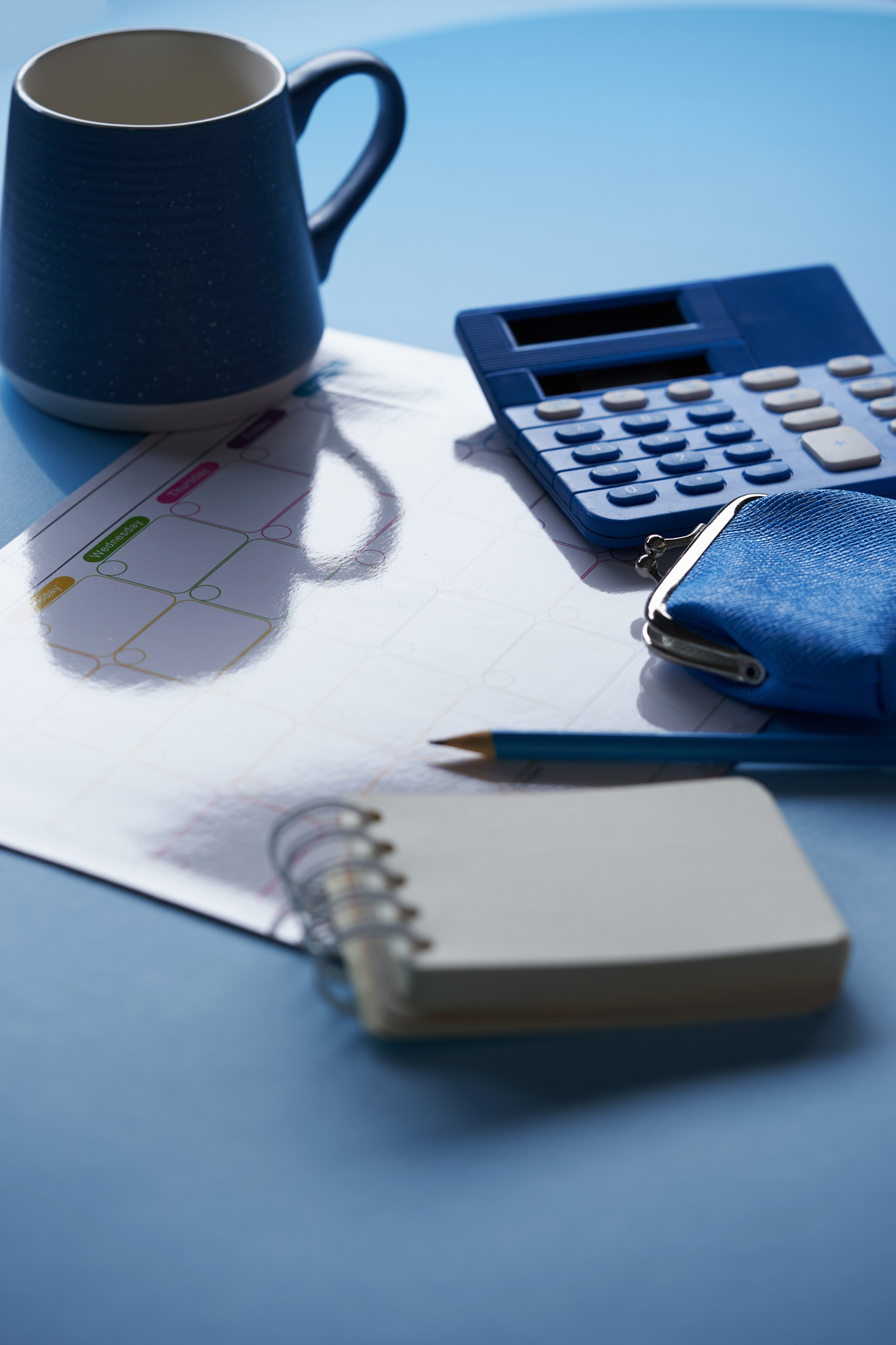 blank monthly planner coin purse calculator and coffee mug against blue background