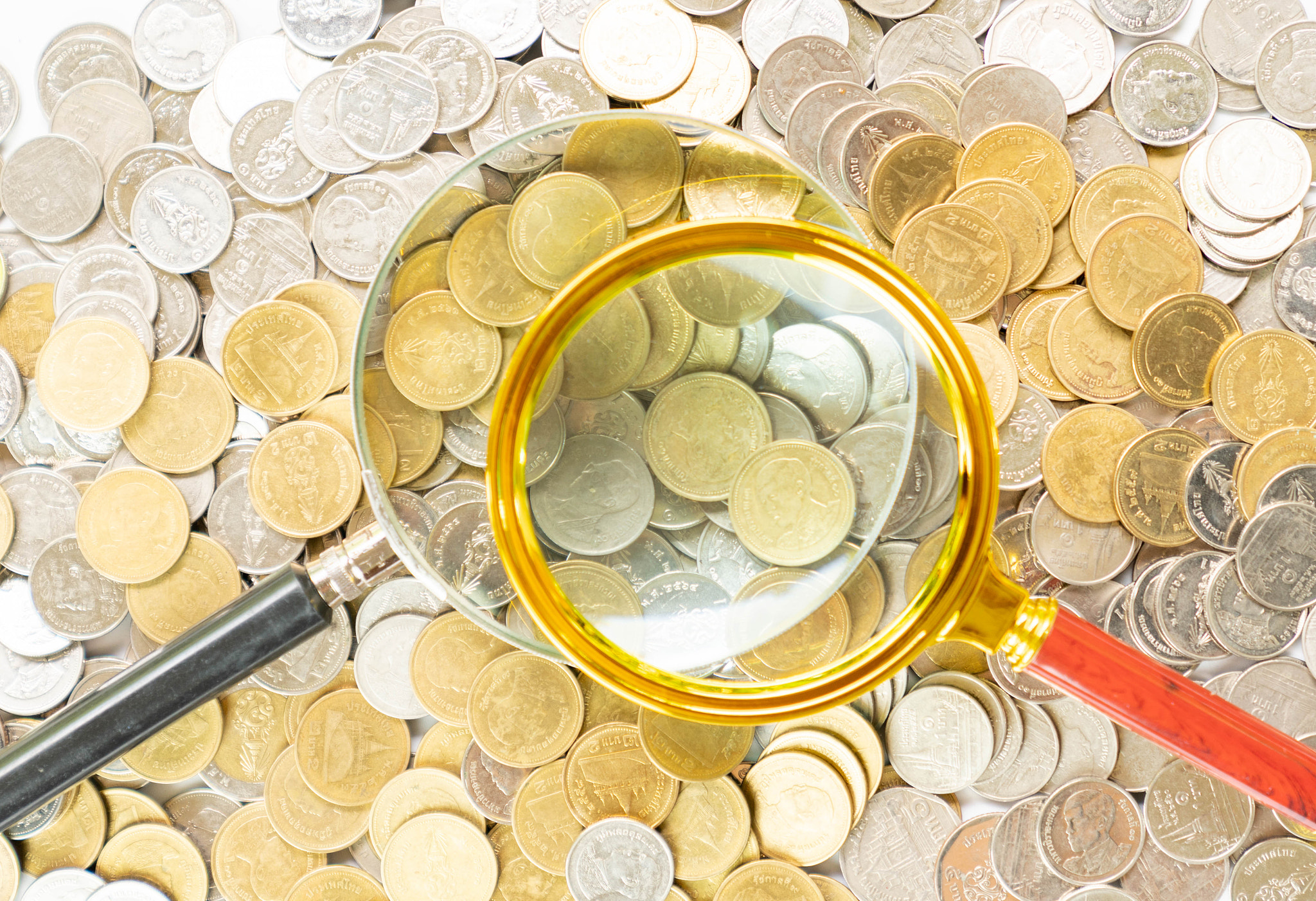 Magnify glass on a pile of money coins.