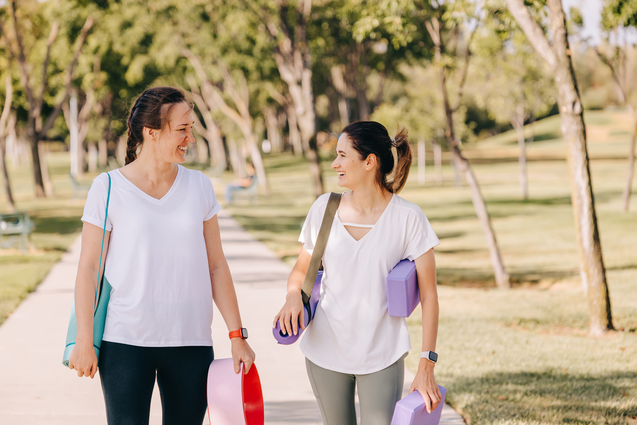 Two young women walking in the morning park, going to do yoga outdoors: Two smiling young women walking in the morning park, going to exercise outdoors. Carrying mats and other equipment for yoga.