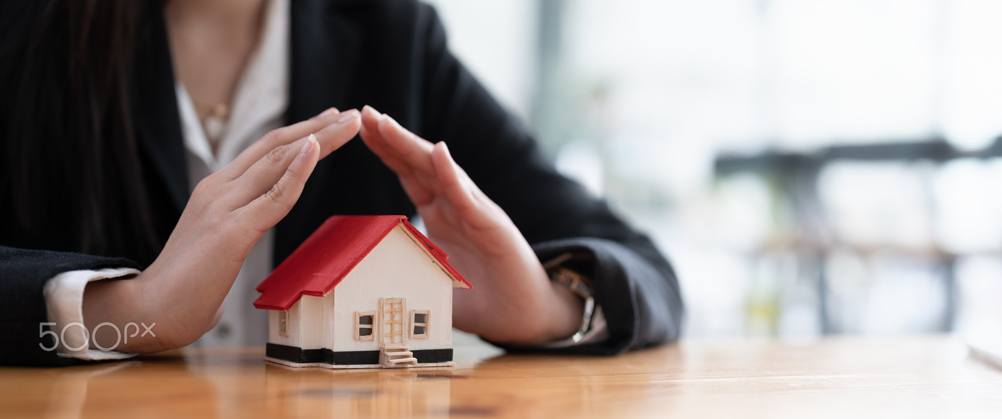 Wooden toy house protected by hands with copy space. Home insurance