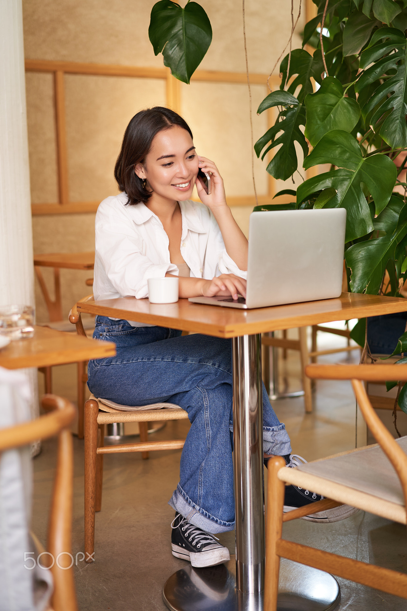 Stylish young woman answer phone call, sitting in cafe with laptop