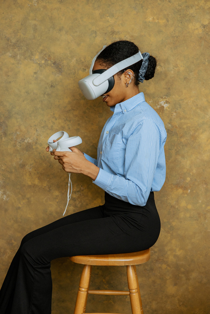 Young woman wearing virtual reality simulator while sitting on chair against wall by Junior Asiama on 500px.com