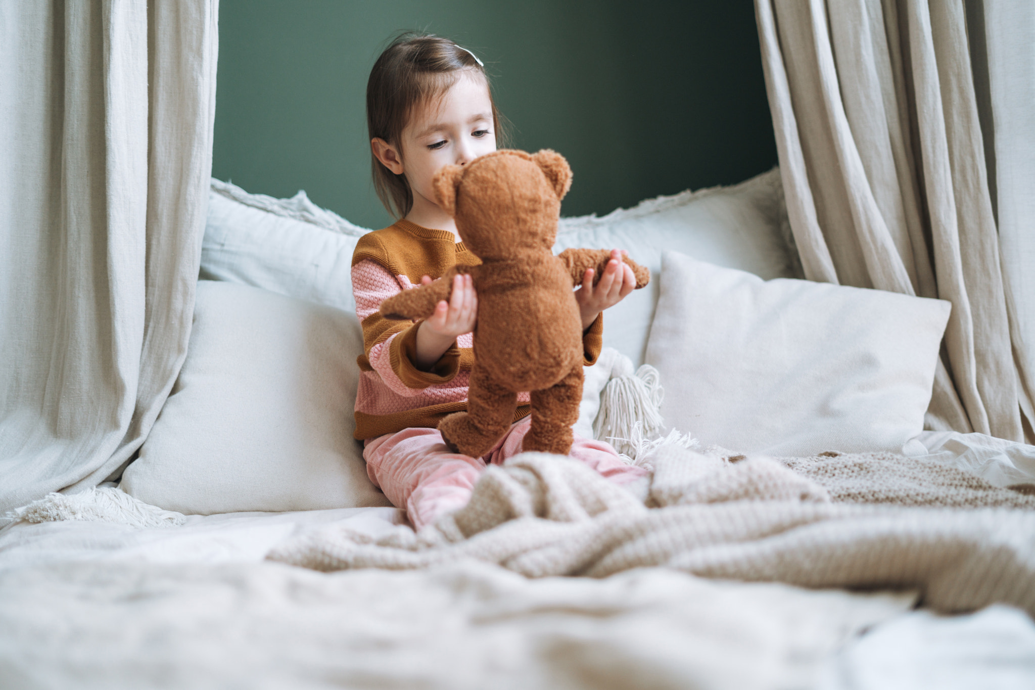 Little girl playing with toy bear in bed room with Christmas tree at home