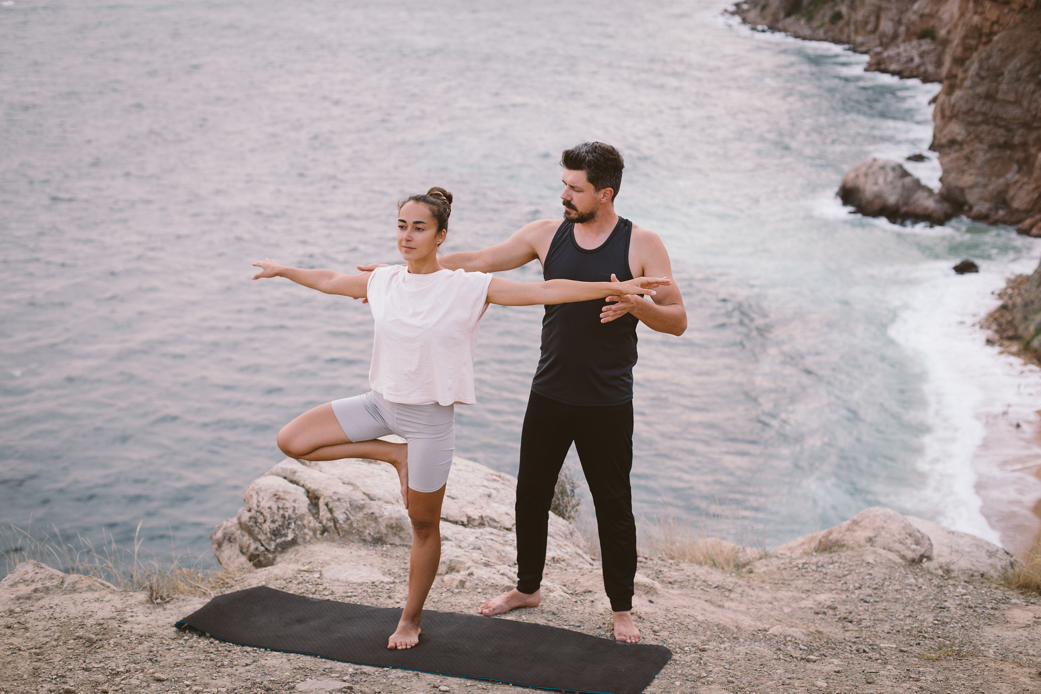 Young man coach teaches woman yoga exercises on an outdoors class