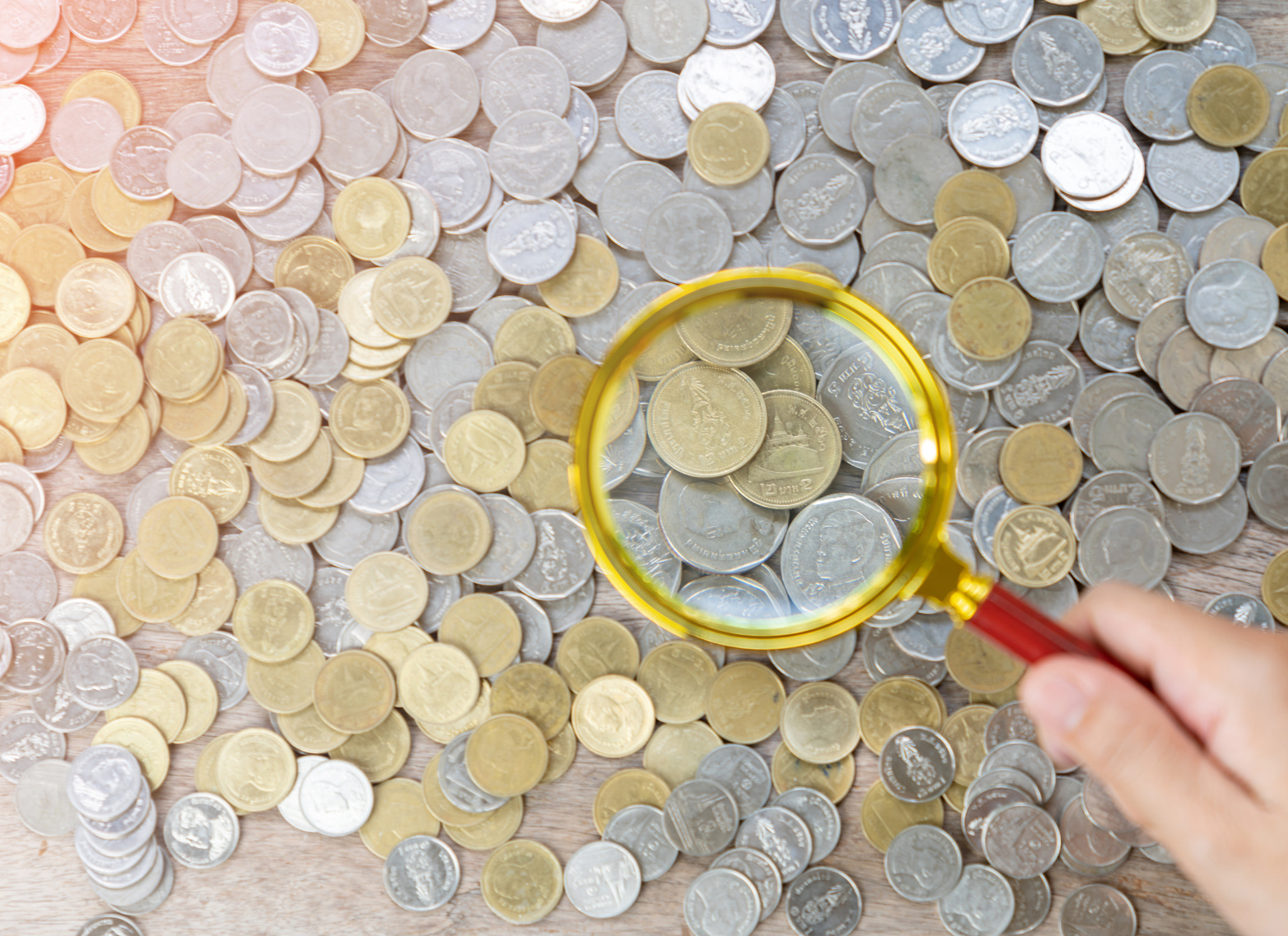 Magnify glass focus on a pile of money coins.