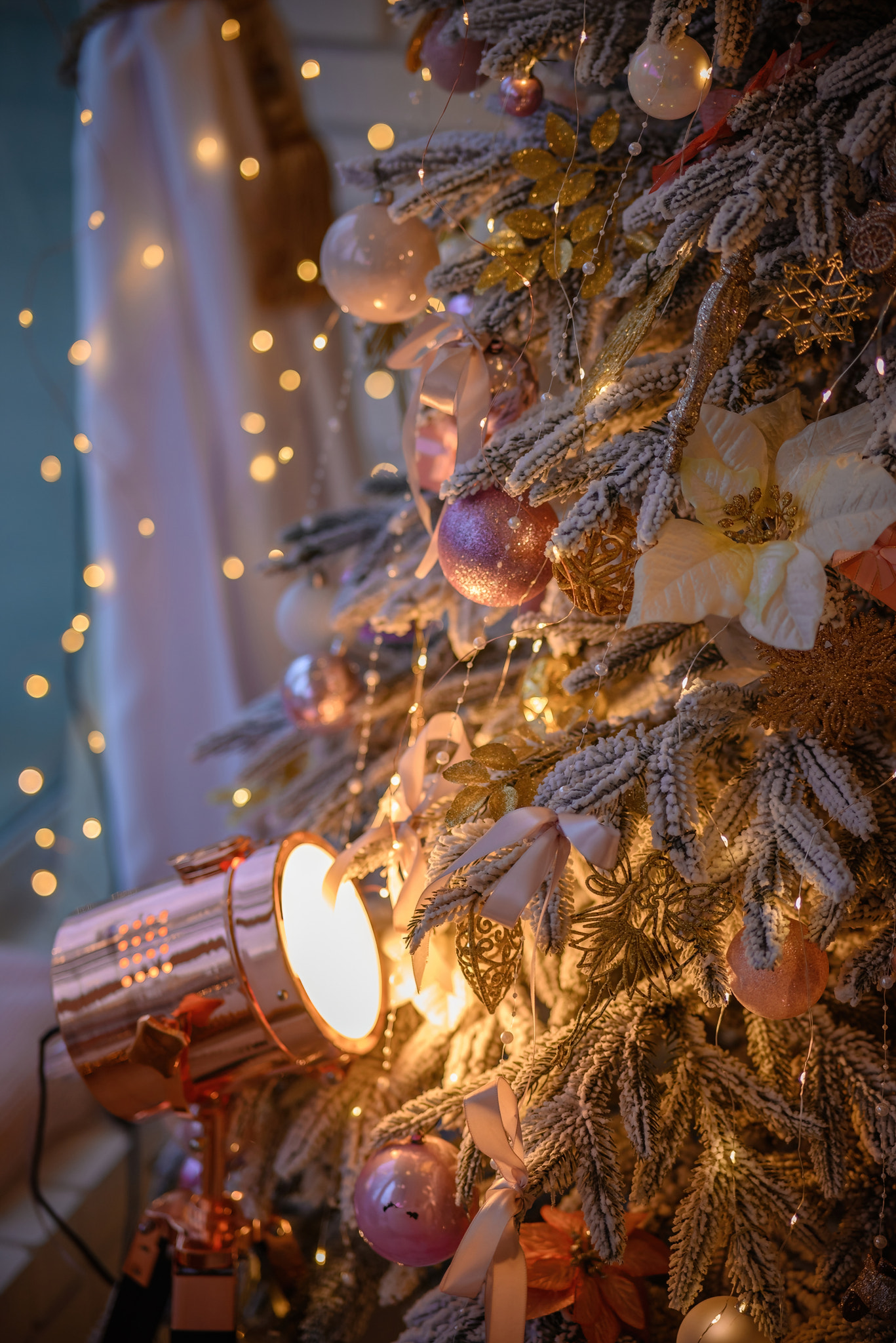 Close-up, branches of Christmas tree with decorations and garland, illuminated by spotlight in room.