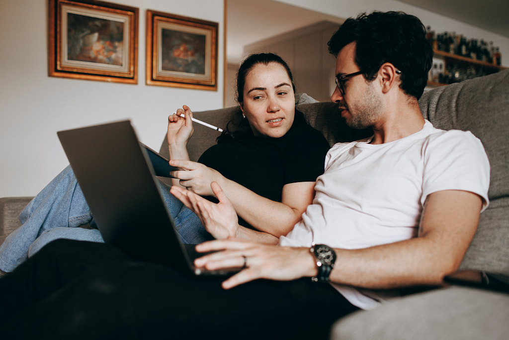 Young couple sitting on sofa and using laptop by Helena Lopes on 500px.com