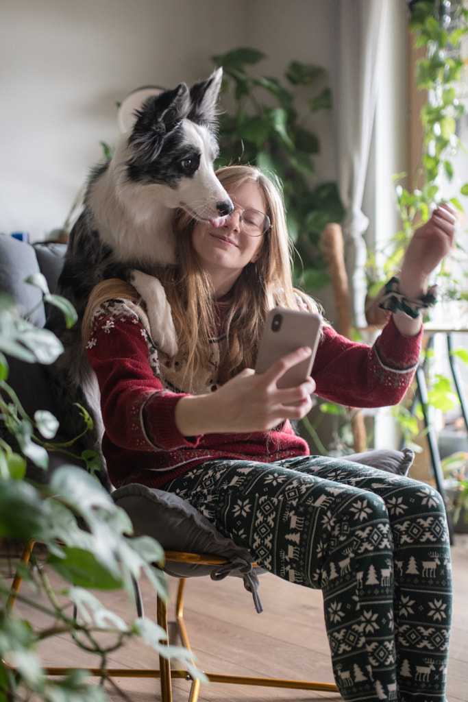 Smiling woman taking funny selfie by mobile phone while sitting on chair with a dog at home by Iza ?yso? on 500px.com