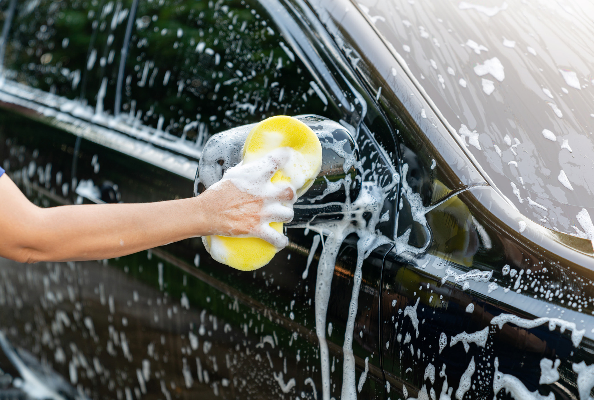 Woman washing black car with sponge on her house.