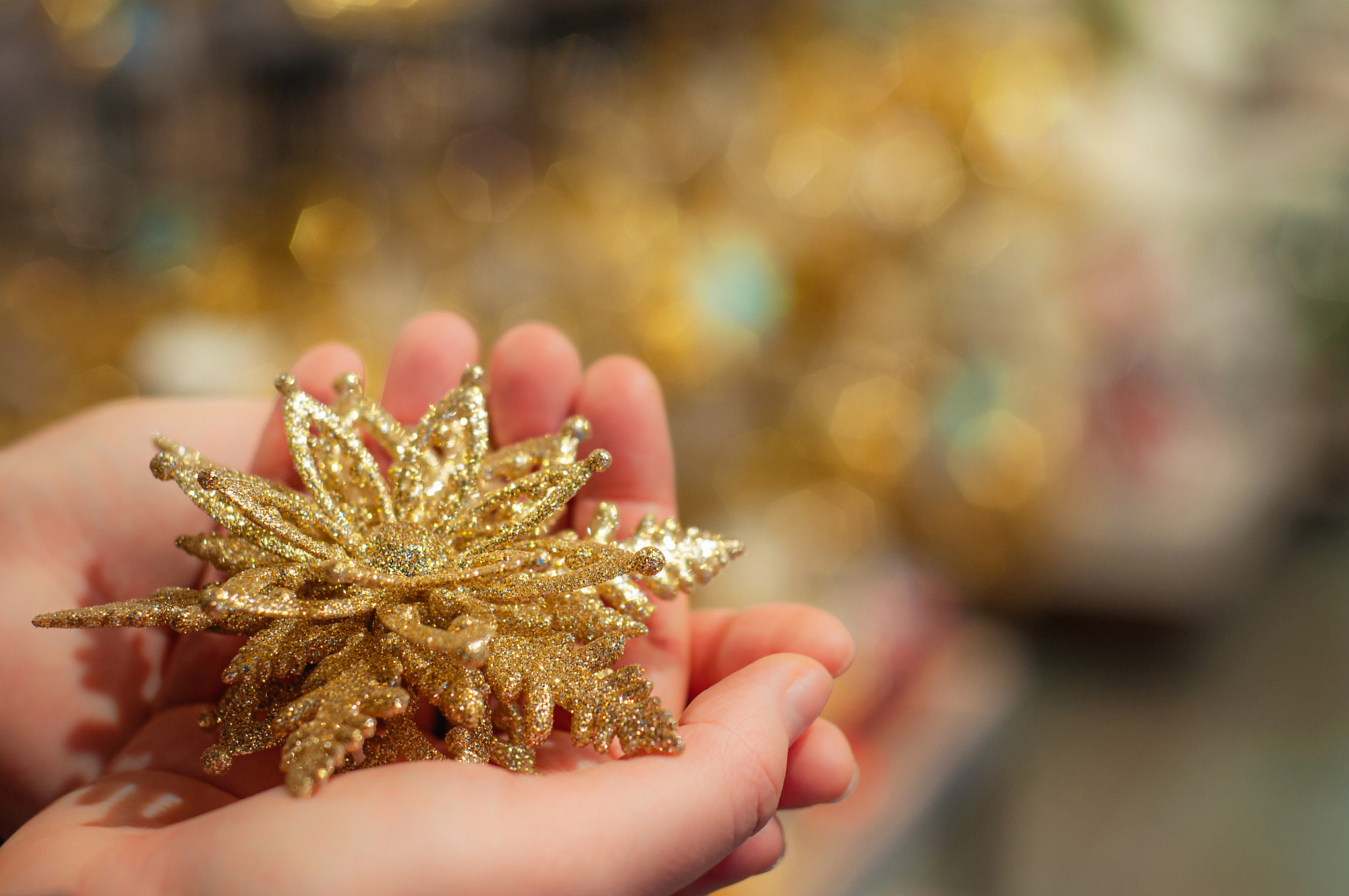 Christmas tree toy in hands. Golden snowflake on defocused background