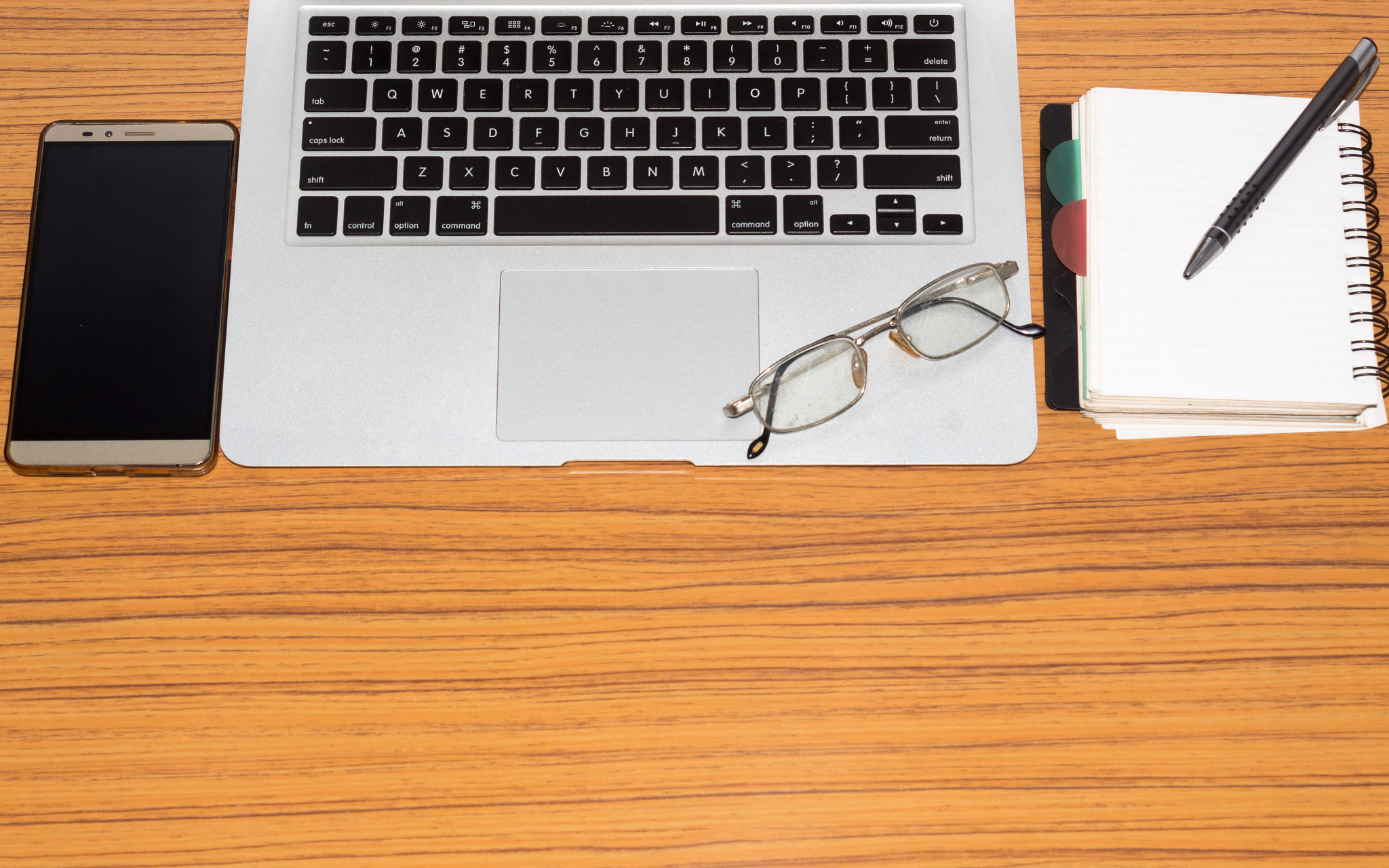 Desk with open notepad, pen, eye glasses, nicely placed on table.