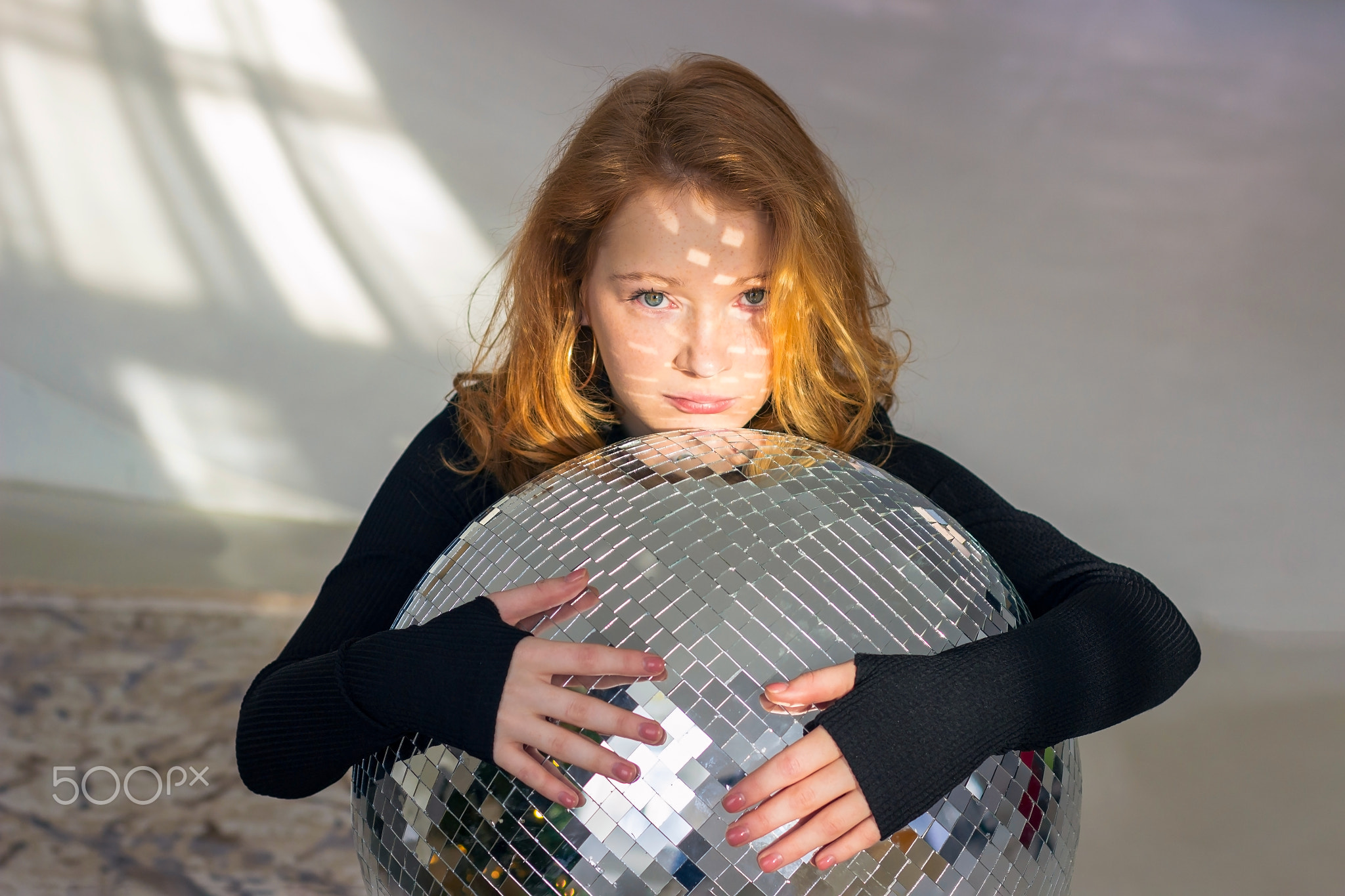 A beautiful young girl model with red hair hugs a disco ball. It