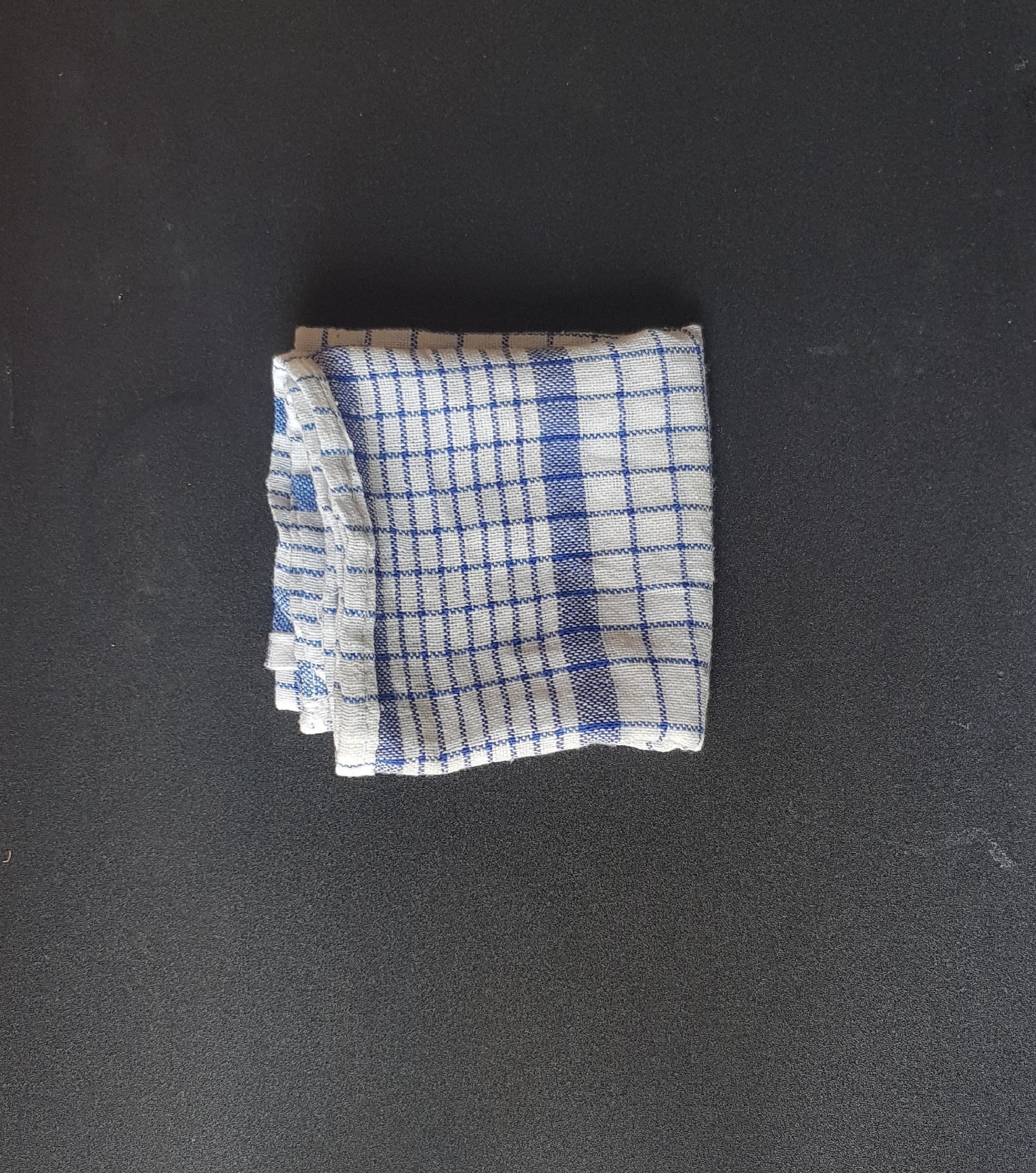 Folded white blue plaid napkin on black board table.