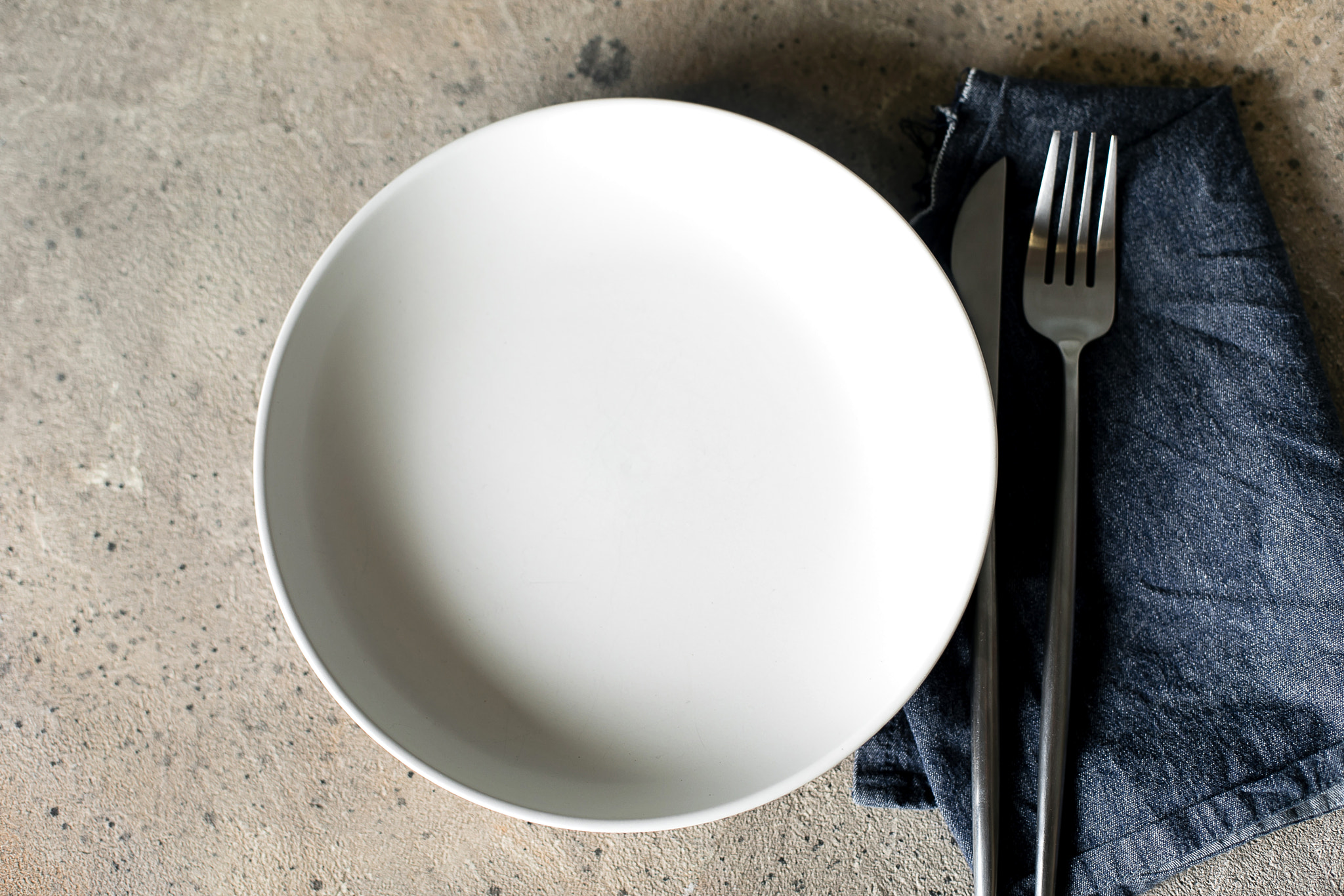 Table Setting Background. Light plate on stone table with blue jeans tablecloth. Top view. Mock up