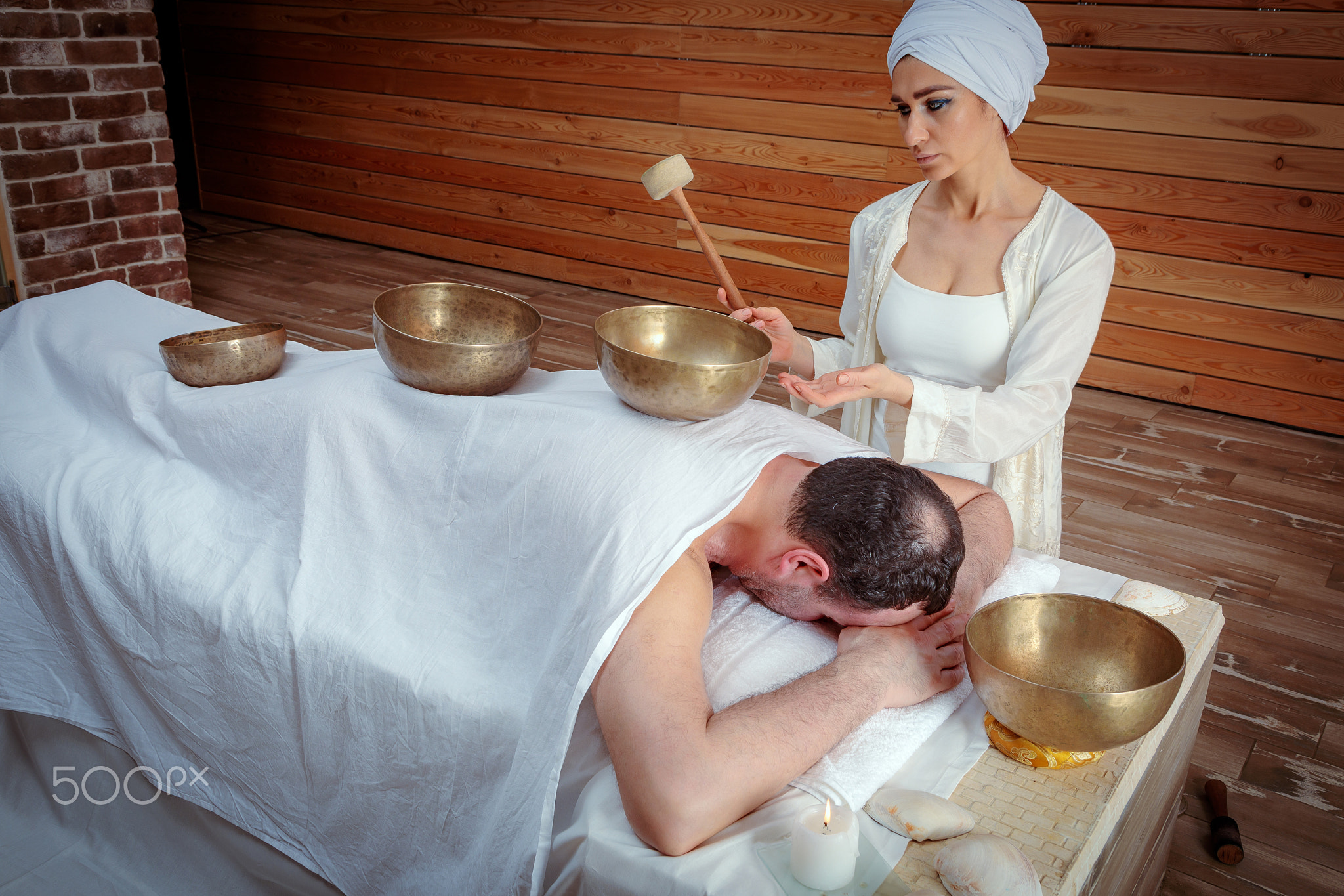 A woman performs Tibetan singing bowl therapy with a man lying under a