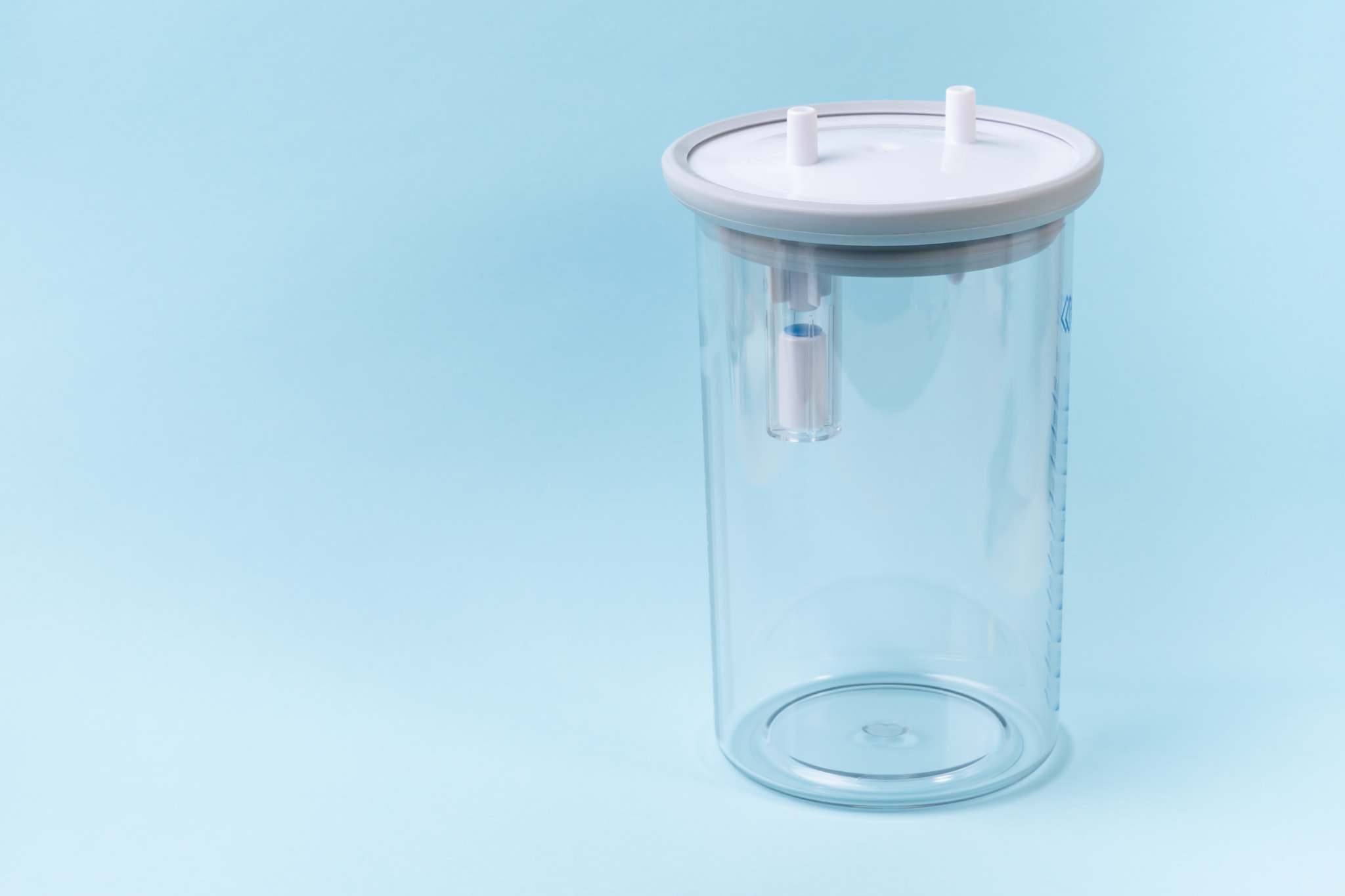 Plastic canister from medical suction machine on blue backdrop