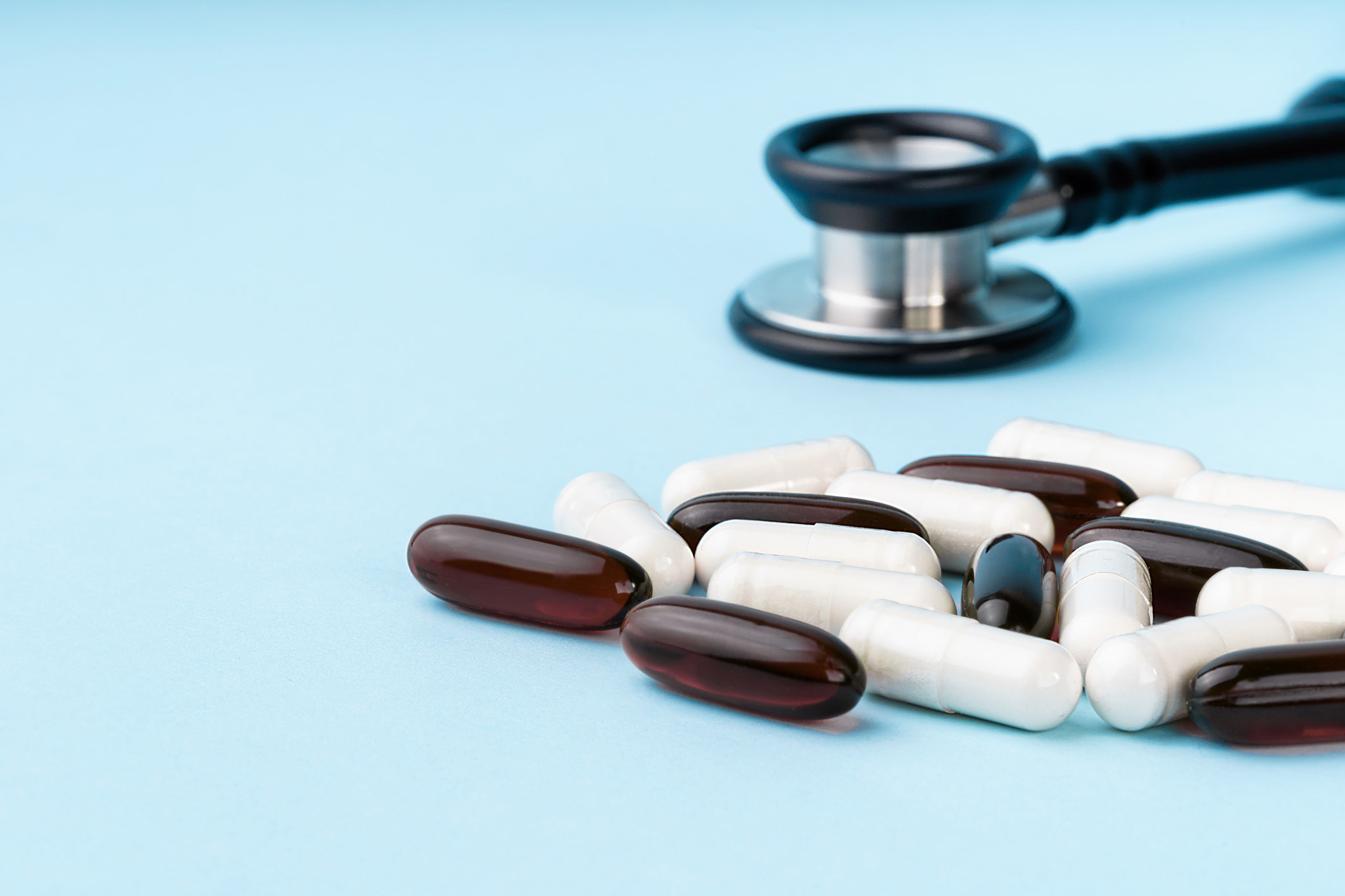 Assorted brown and white capsules, stethoscope, pills, isolated on blue background.