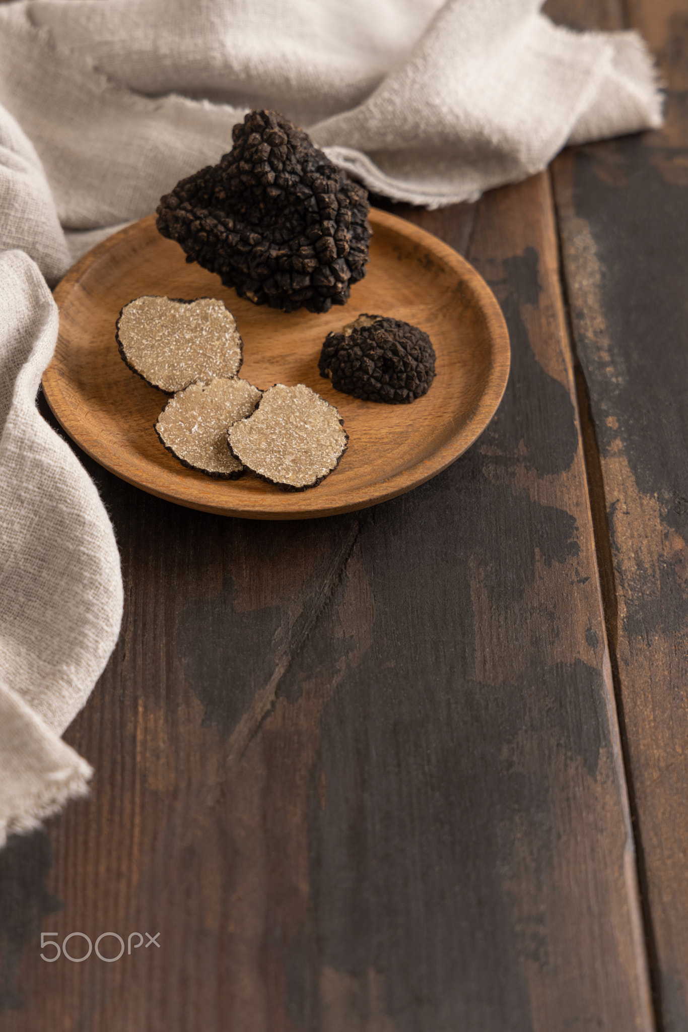 Whole and sliced black truffles mushroom on wooden plate on dark brown table, close up, copy space