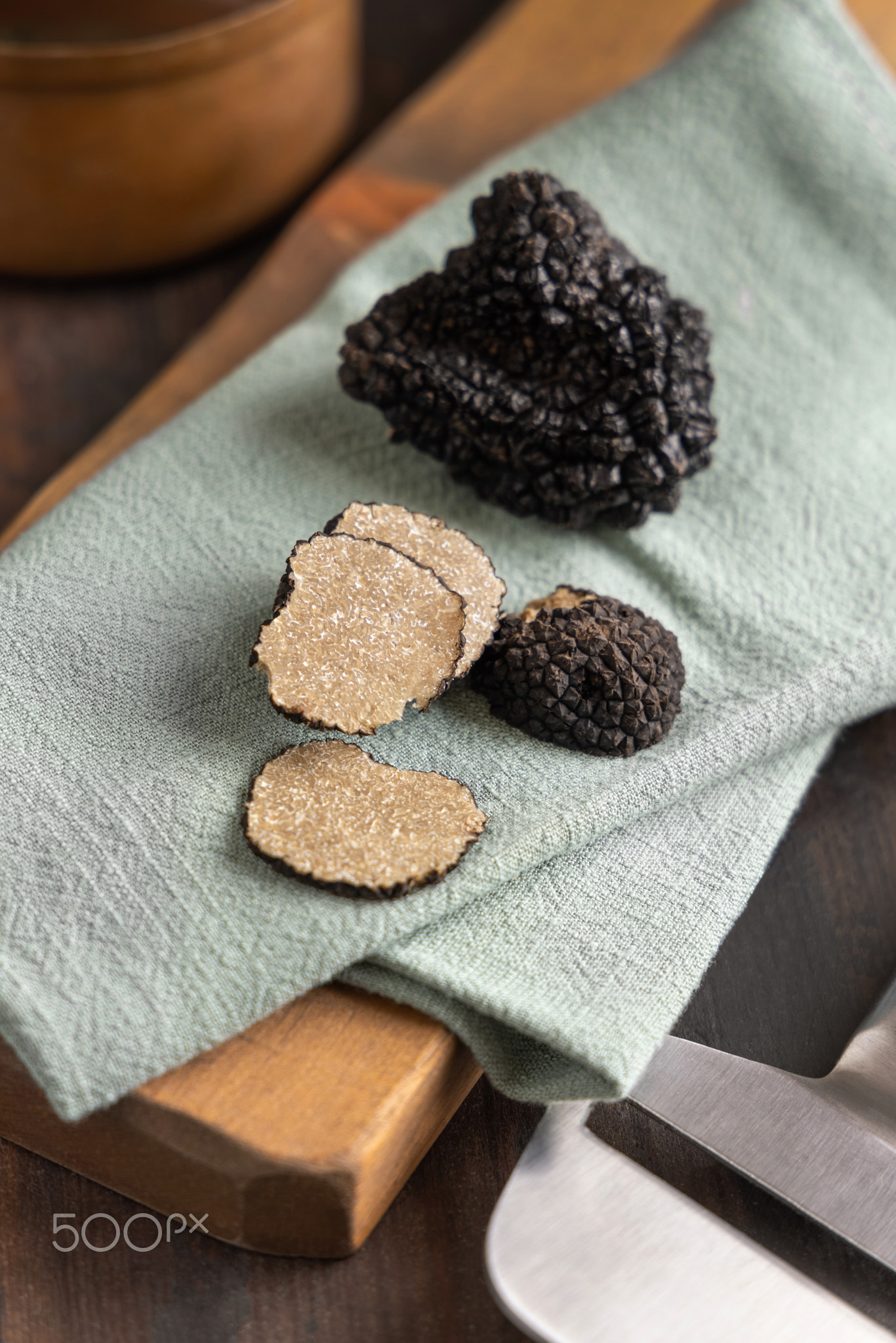 Whole and sliced black truffles mushroom on wooden board on green napkin, close up